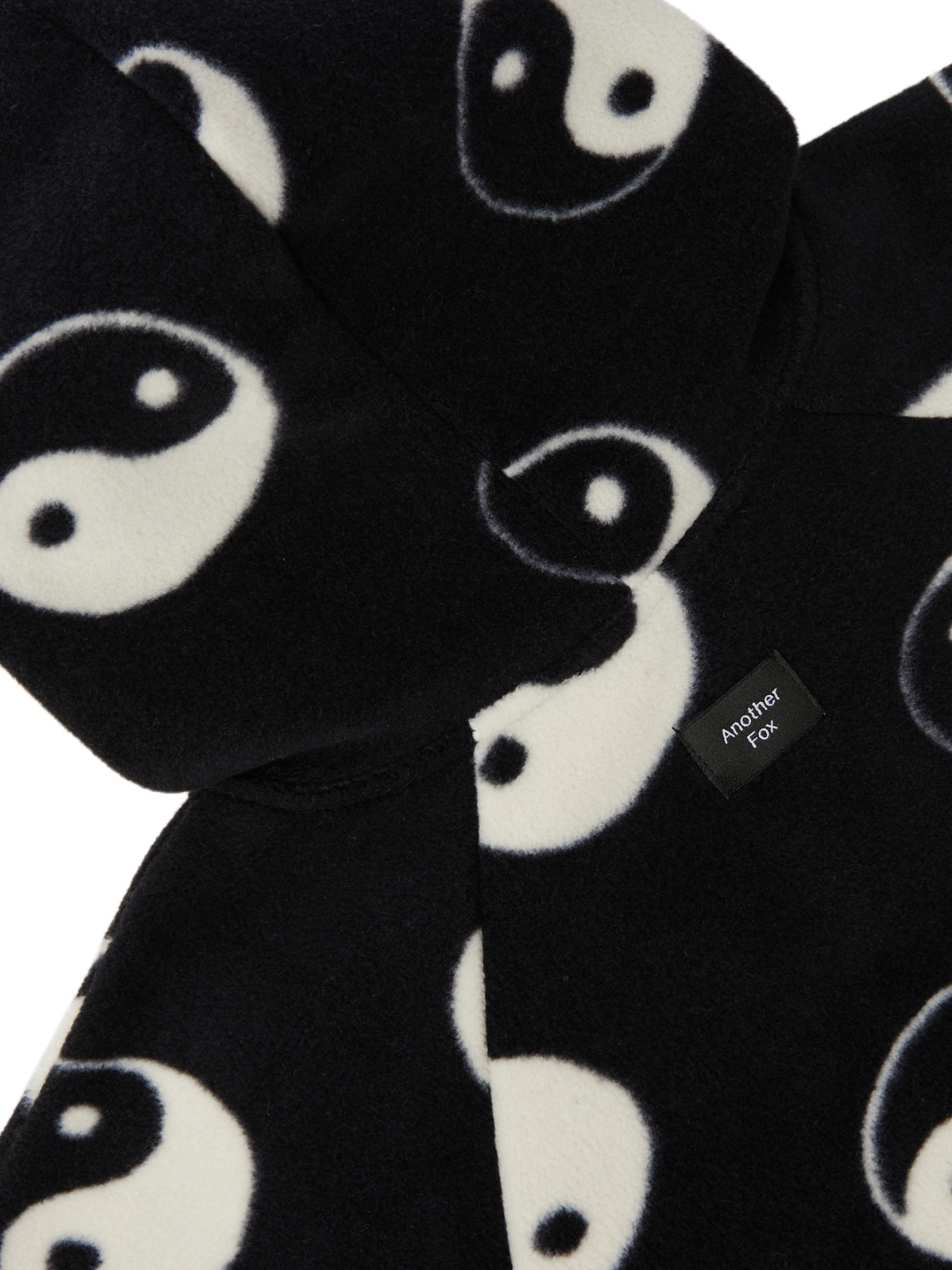 Close-up of the YIN YANG FLEECE STROLLER SUIT, a black garment adorned with a pattern of white yin-yang symbols, featuring a small label that reads "Another Fox." Perfect for your baby's wardrobe, this piece is one of our exciting new arrivals in clothing.