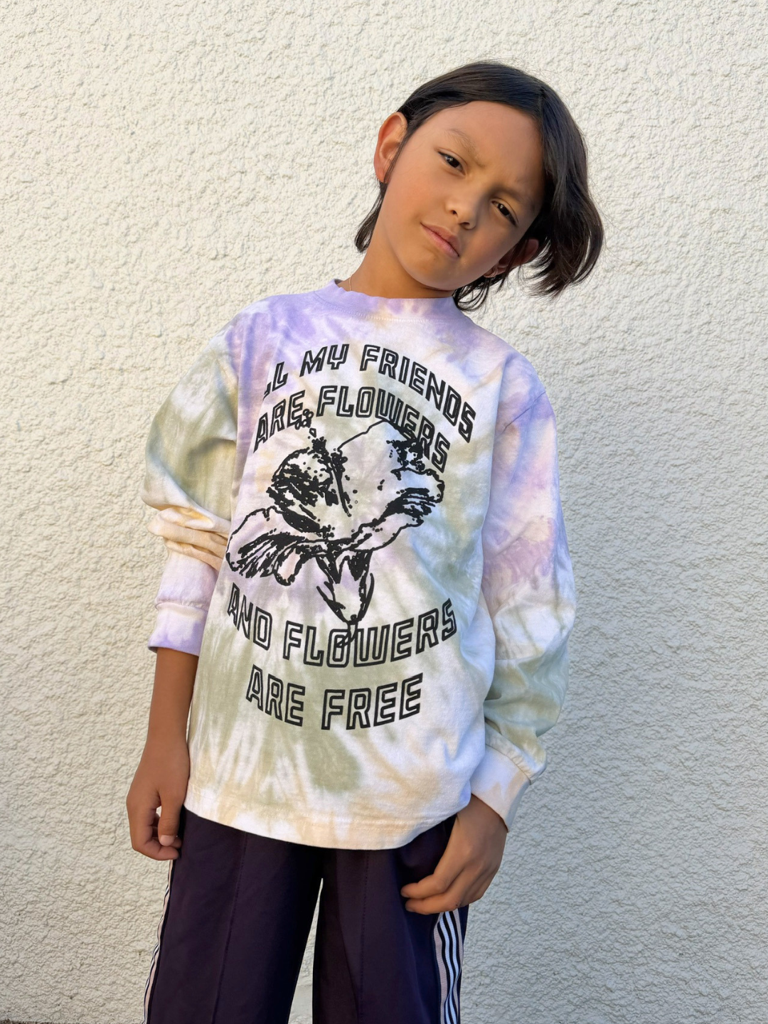 Child wearing a tie-dye shirt with text and graphic design against a plain background