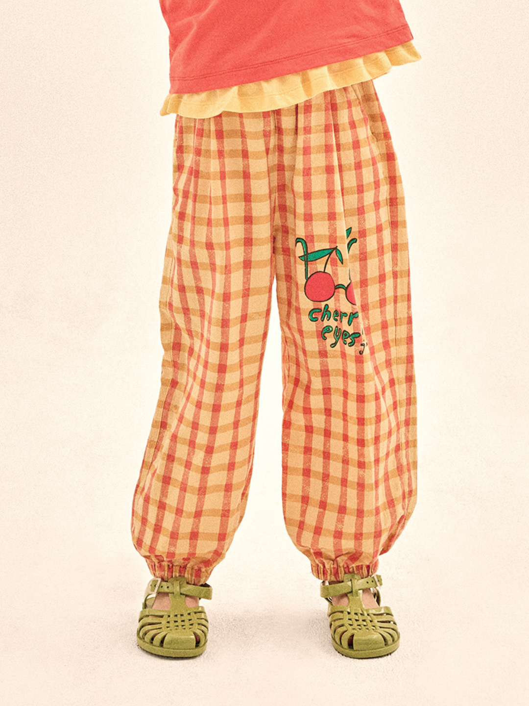 Checkered pants with cherry design and text on a beige background
