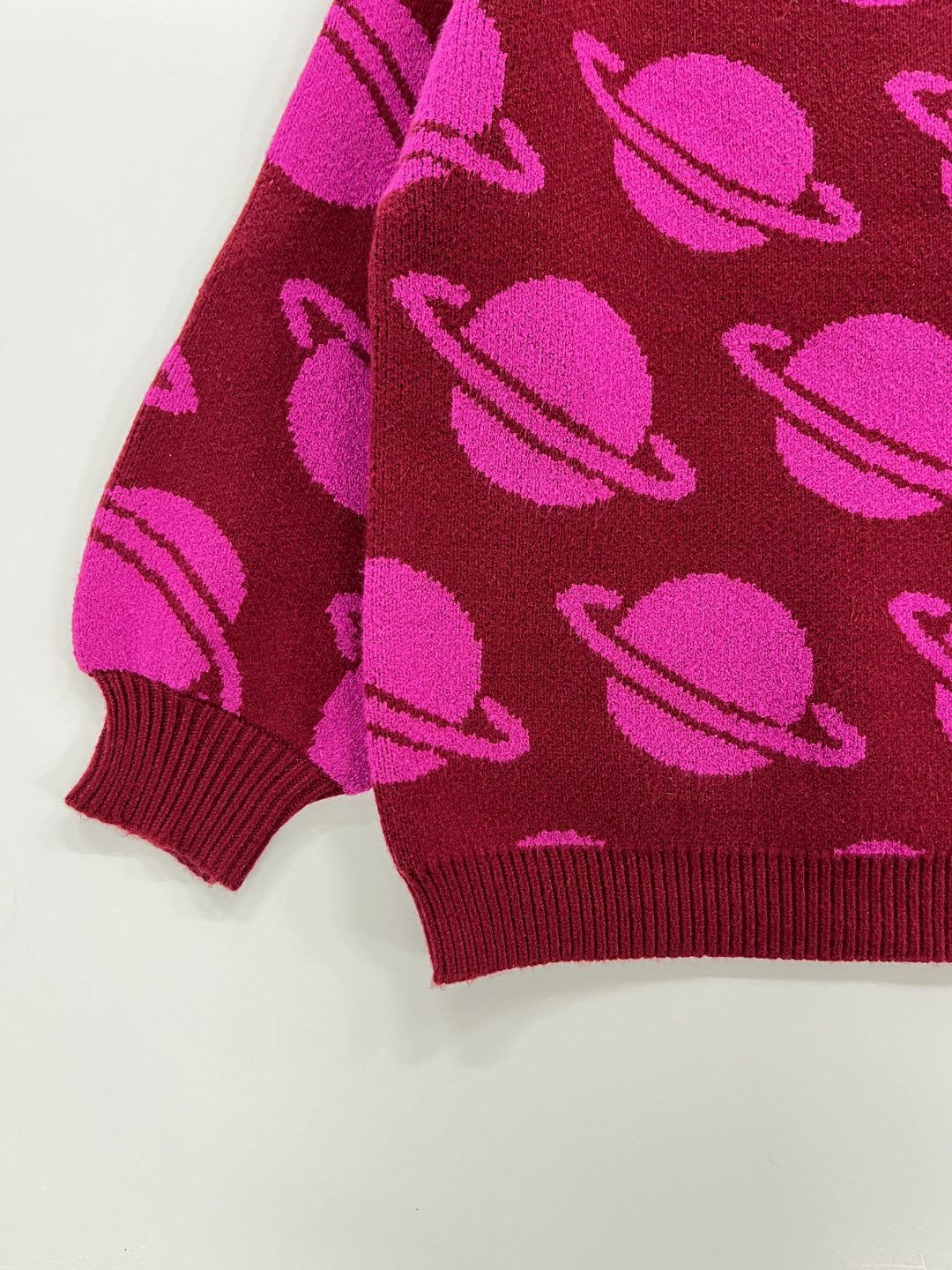 Maroon | A close-up view of the SPACE CAMP SWEATER, featuring intricate pink Saturn planet designs on a vivid red background.