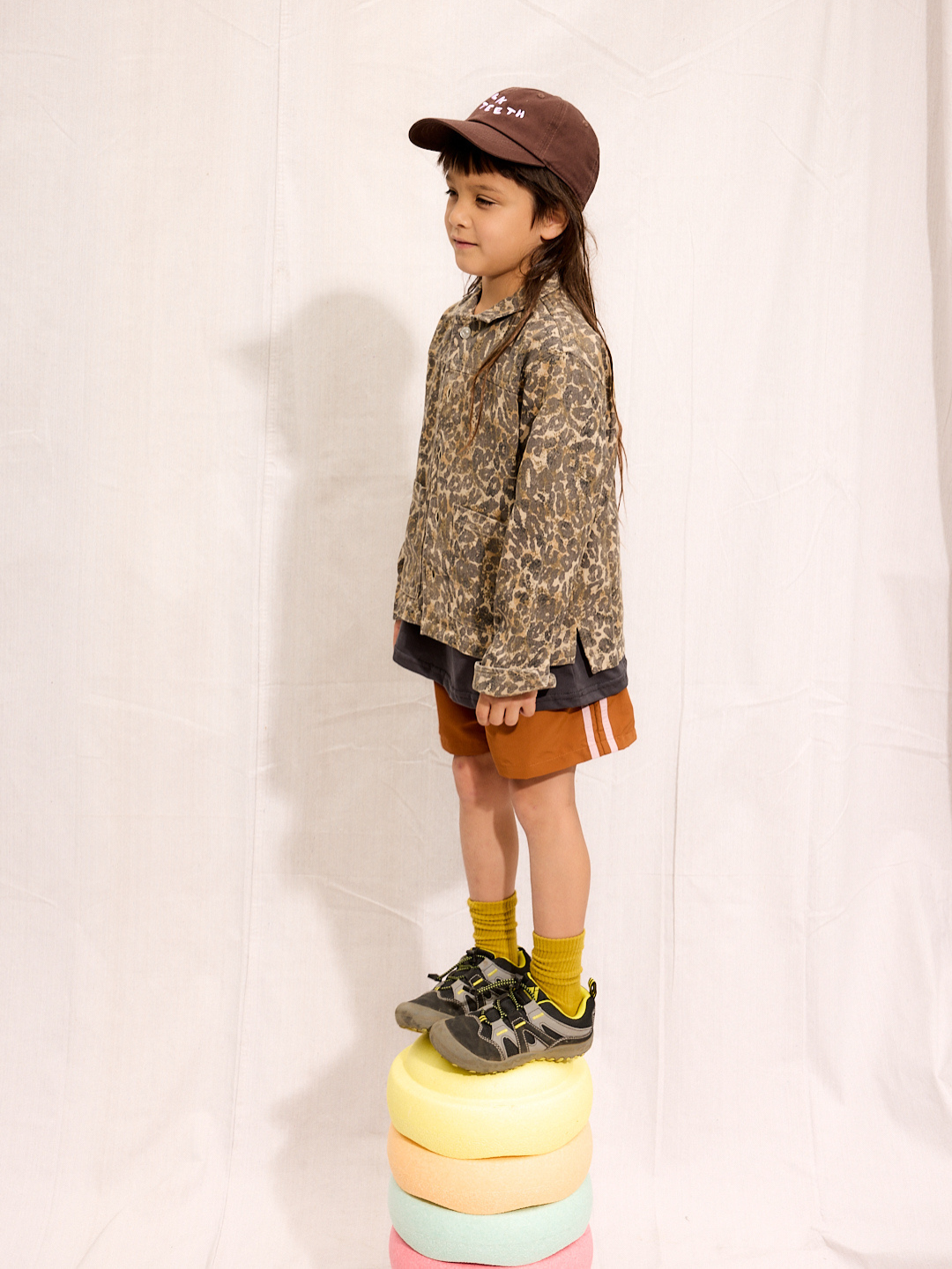 Rust | A child is wearing the rust Sprinter Shorts with a leopard jacket and Milk Teeth Hat