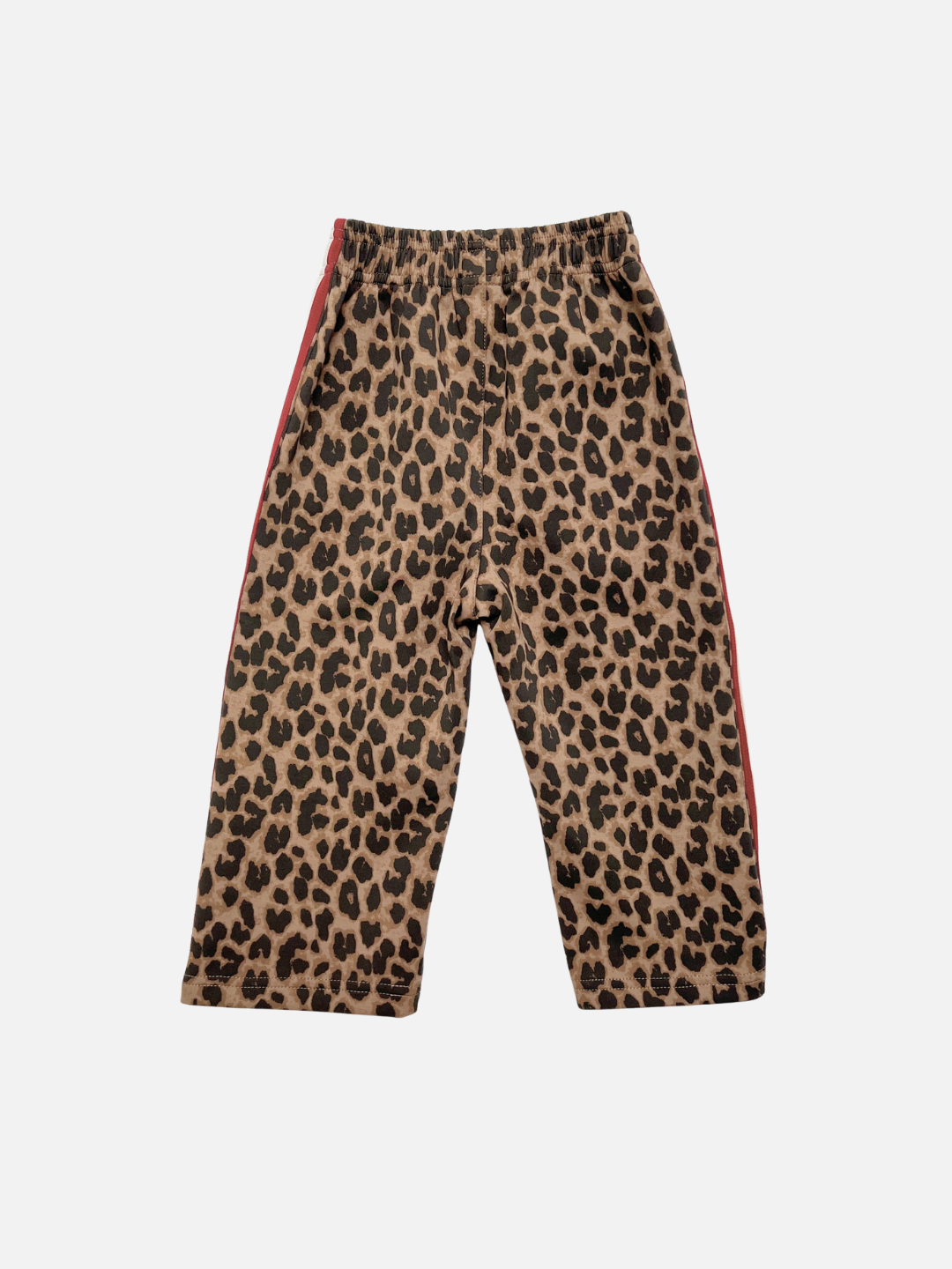 Back view of a pair of children's leopard print pants with a tan and brown base, black spots, and a red side stripe, shown flat against a light gray background.
