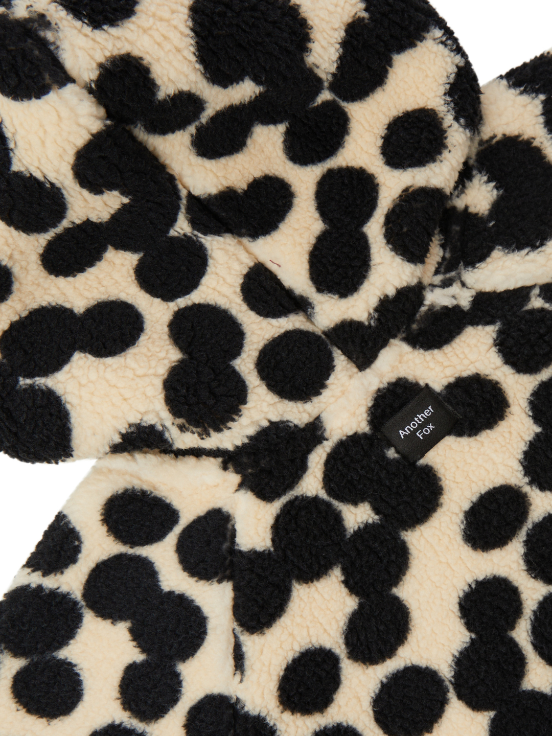 Close-up of a cream and black spotted fleece fabric with a label that reads "Another Fox," perfect for baby and new arrivals collections, featuring the SPOT STROLLER SUIT.