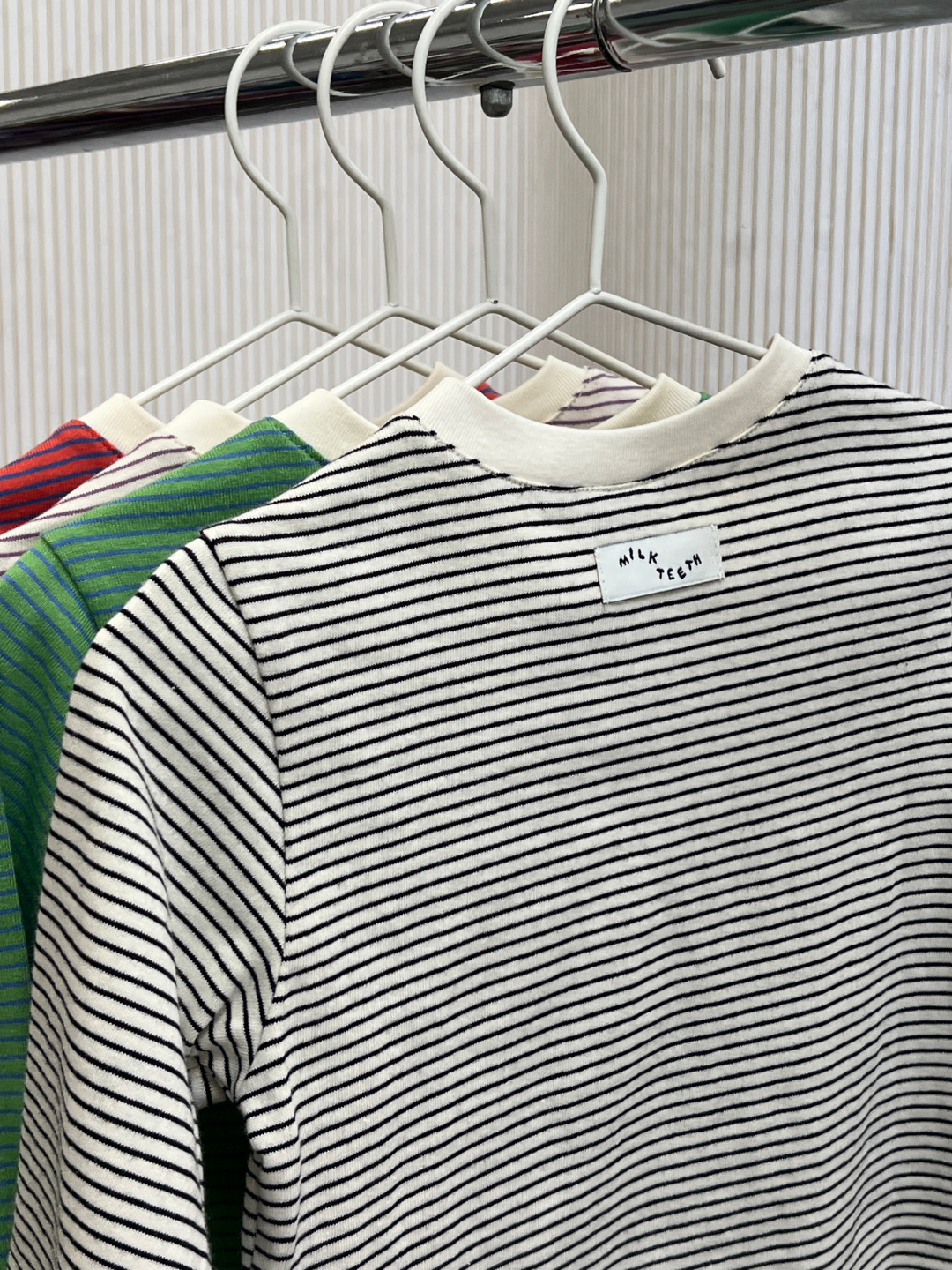 White/Black | Four BABY STRIPE LONGSLEEVE shirts in an assortment of colors hang on white hangers from a metal rack; the front shirt features black and white stripes with a small “NIK TECH” label on the back. Crafted from soft cotton jersey, these baby and toddler essentials offer easy dressing and all-day comfort.
