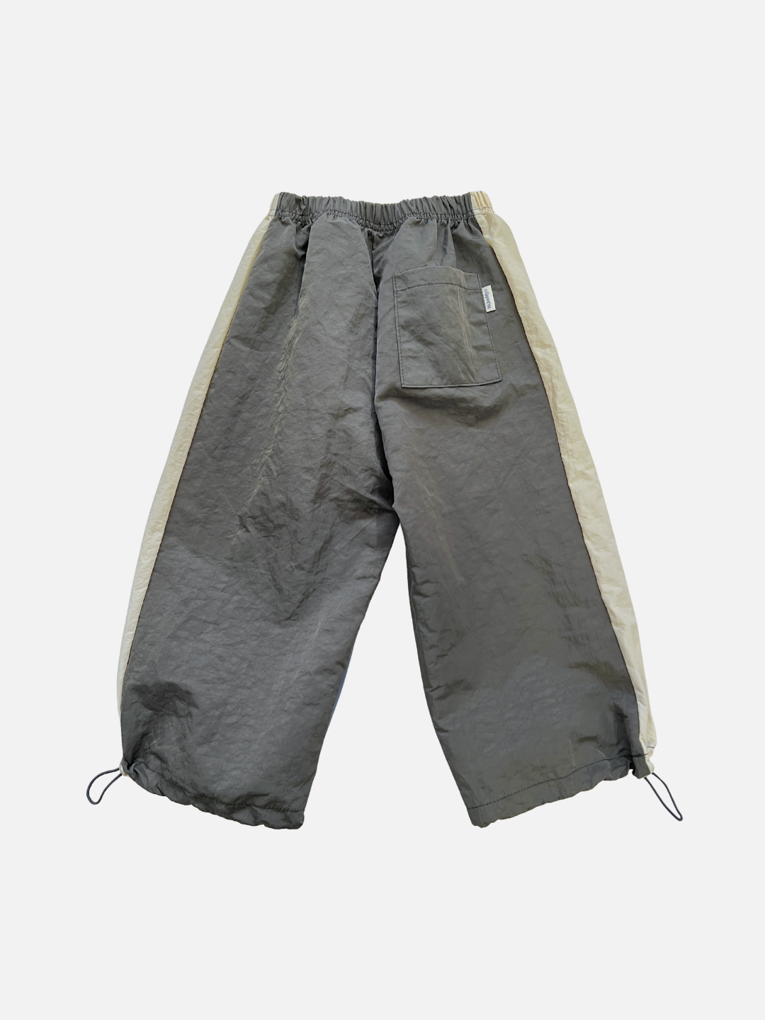 The WARM-UP PANT is a pair of loose-fitting gray jogger pants with beige side panels, an elastic waistband, ankle drawstrings, and a back pocket—a stylish choice from a Korean kids brand, shown on a white background.