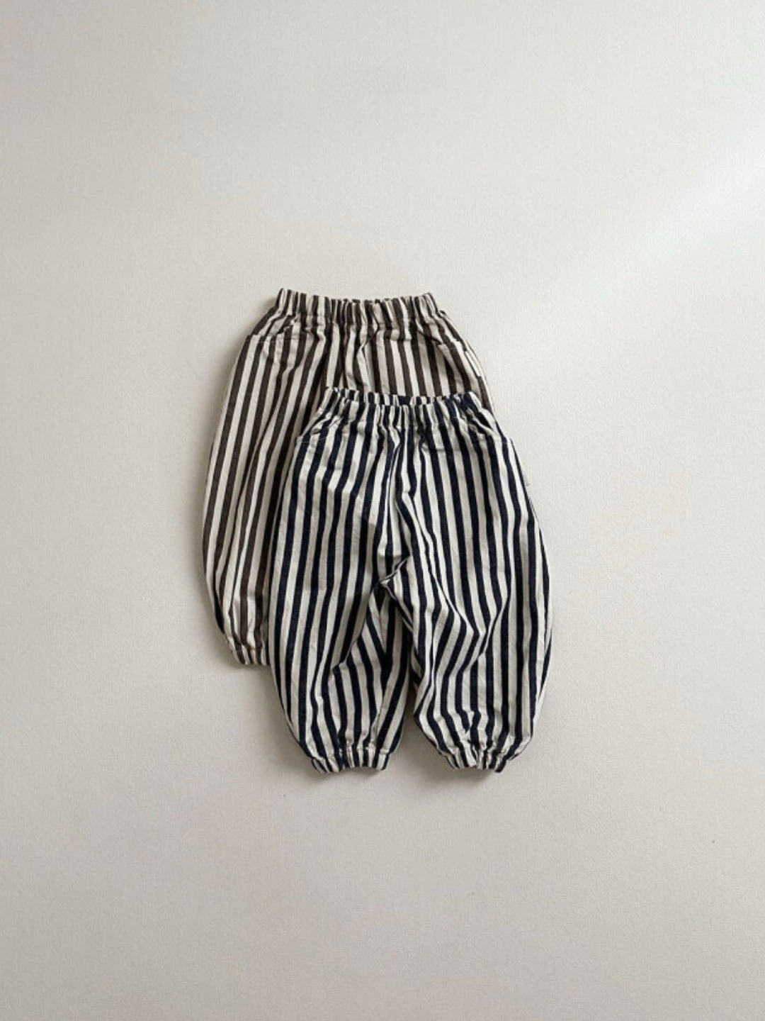 Navy Stripe | Two pairs of PIRATE PANTS by Minirobe, showcasing cotton material with elastic waistbands and cuffs and balloon legs: one pair featuring black and white stripes and the other brown and white stripes, laid flat against a plain background.