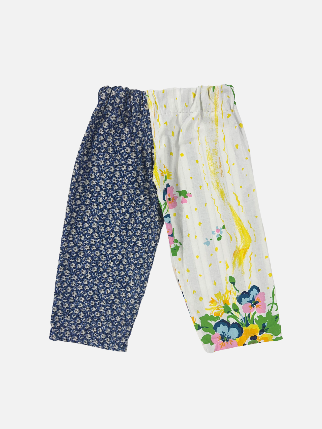 Front view of kid's patchwork pant. Left leg - white flower on navy. Right Leg - yellow splashes and flowers. 