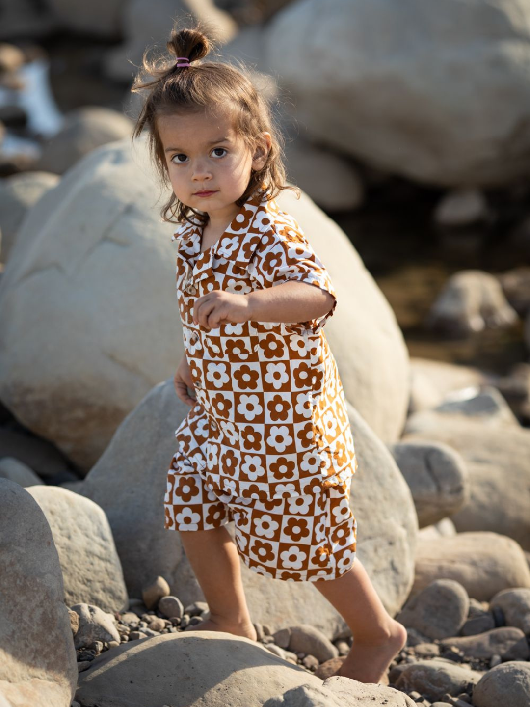 Child climbing over rocks wearing a kids' shirt and shorts set in a checkerboard pattern of terracotta brown and white flowers