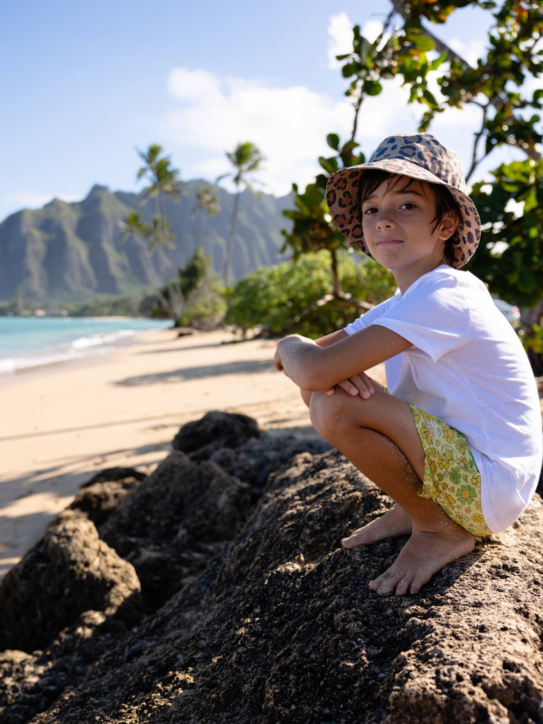 A child is wearing Calico Crab Bucket Hat at the beach, with a white tee and swim trunks.