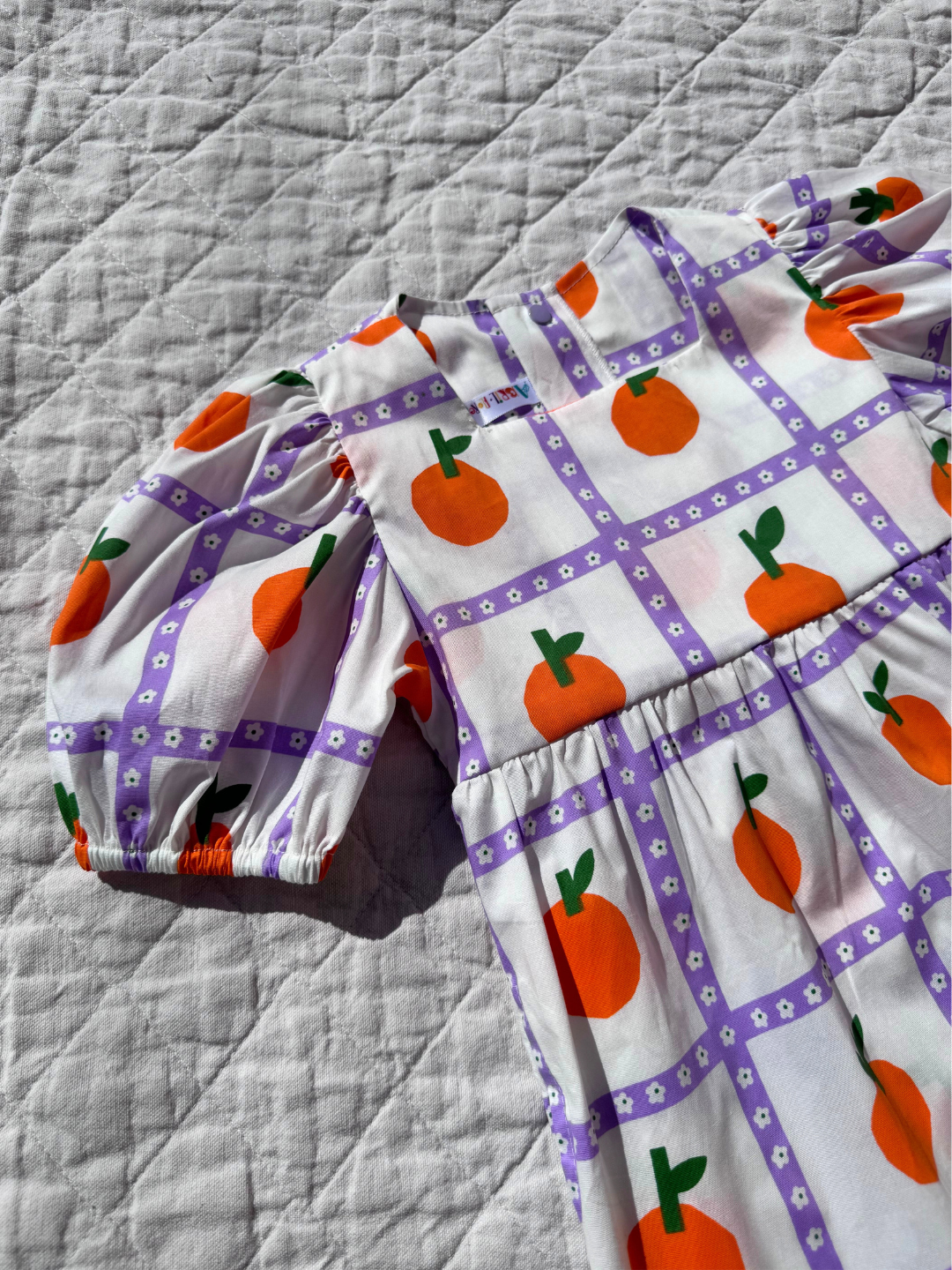 Oranges | A close up of the kid's Glow dress with an all-over oranges print