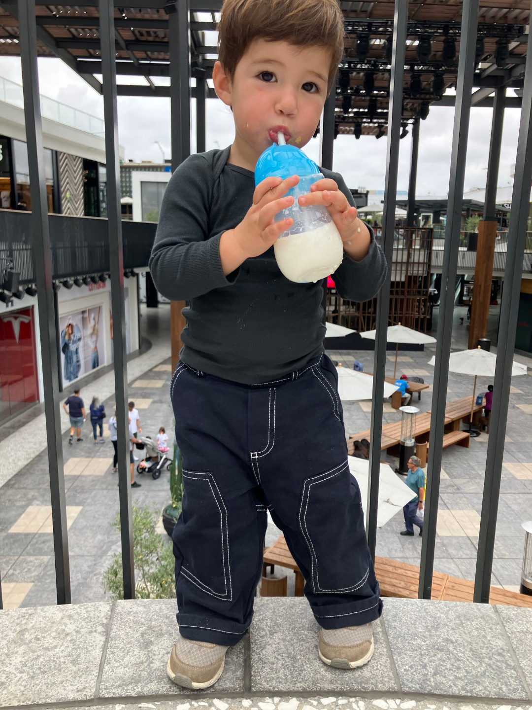 A child is wearing Dark Indigo Stitch Jean with beige sneakers and black top, while drinking milk