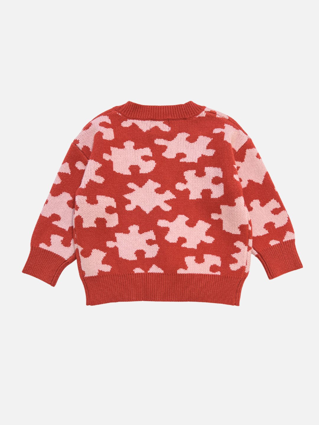 The PUZZLE CARDIGAN is a red knit sweater with a light pink puzzle piece pattern, long sleeves, and ribbed cuffs, hem, and neckline, shown laid flat on a white background.