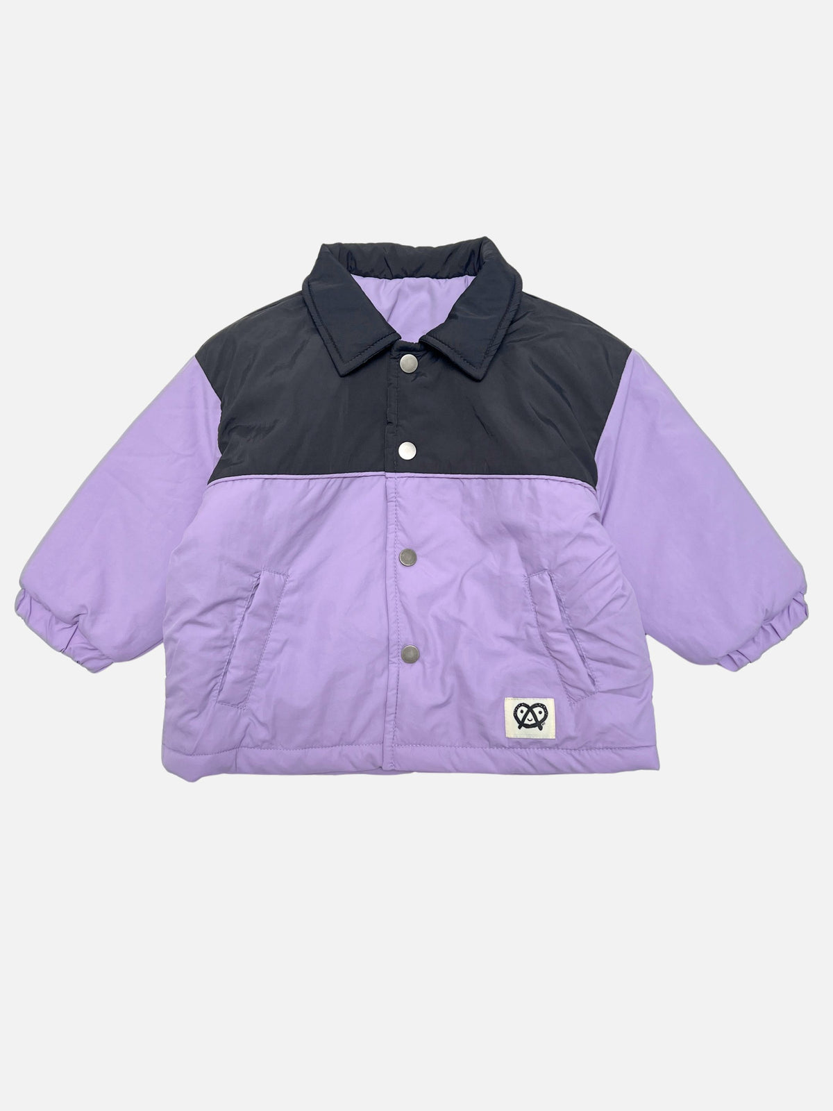 A color-blocked kids puffer jacket with a black yoke and lavender-purple sleeves and body, featuring a snap front and a small pretzel logo patch on the lower left front.