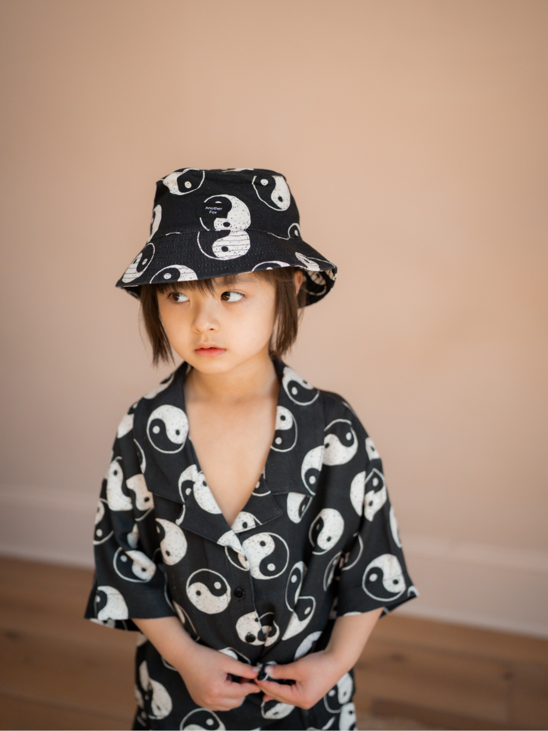 A front view of the black cotton bucket hat with a yin and yang pattern all over on a child.