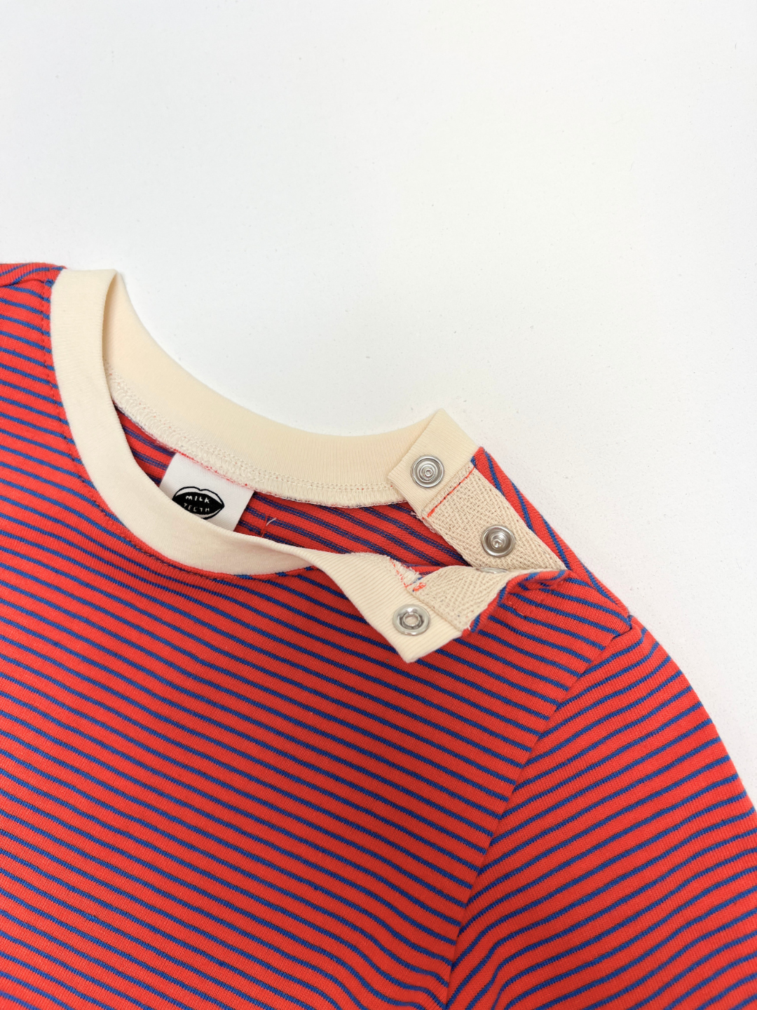 BABY STRIPE LONGSLEEVE features red and blue stripes with a beige collar and convenient shoulder snap buttons, crafted from soft cotton jersey for easy dressing—an ideal basic for babies and toddlers, displayed on a white background.