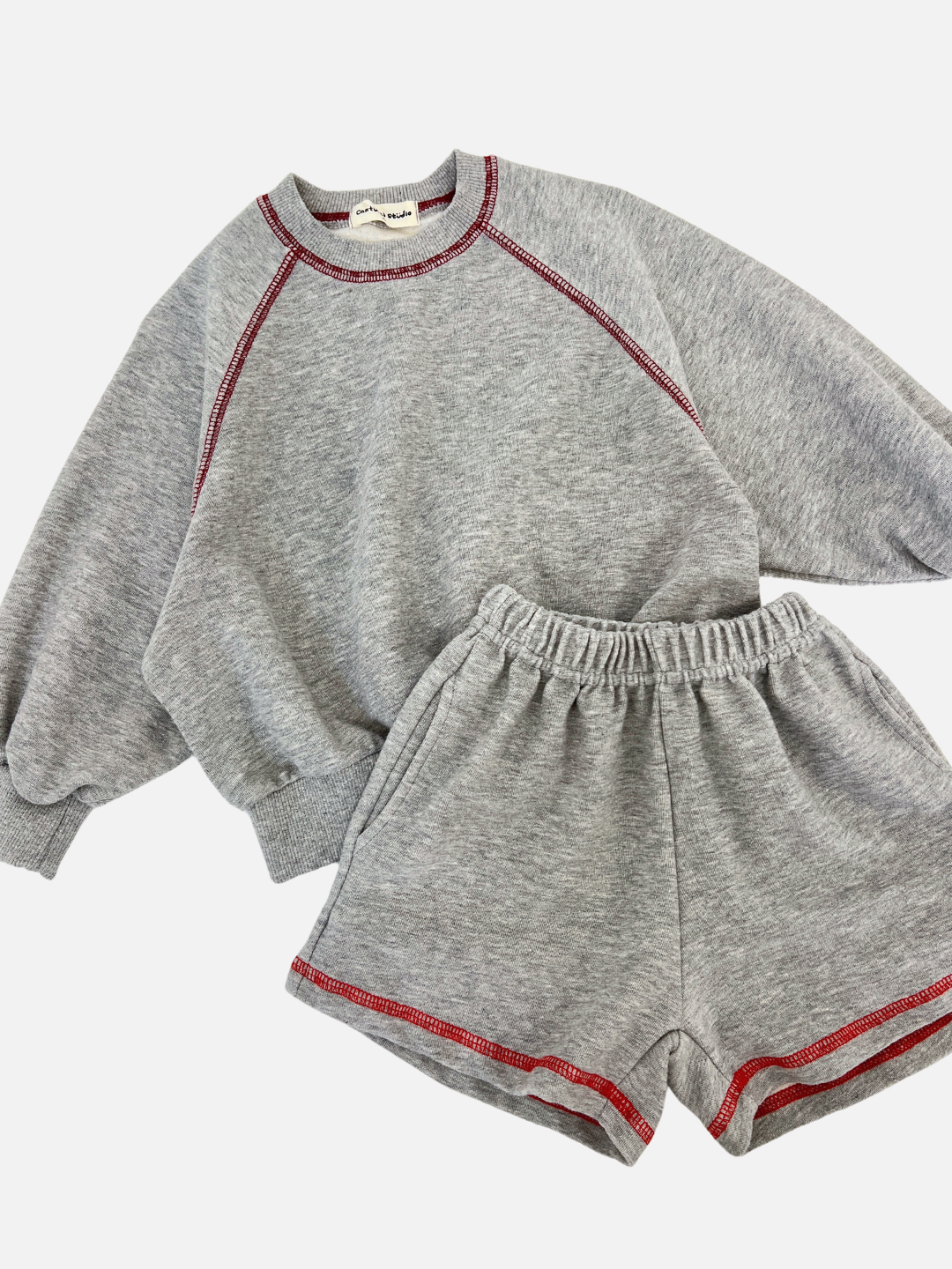 Grey | The VARSITY SWEAT SHORTS set includes a gray sweatshirt and shorts with red stitching, made from brushed cotton for comfort. The sweatshirt has a vintage fit, and the shorts feature an elastic waistband, showcasing the unique style of a Korean kids brand.