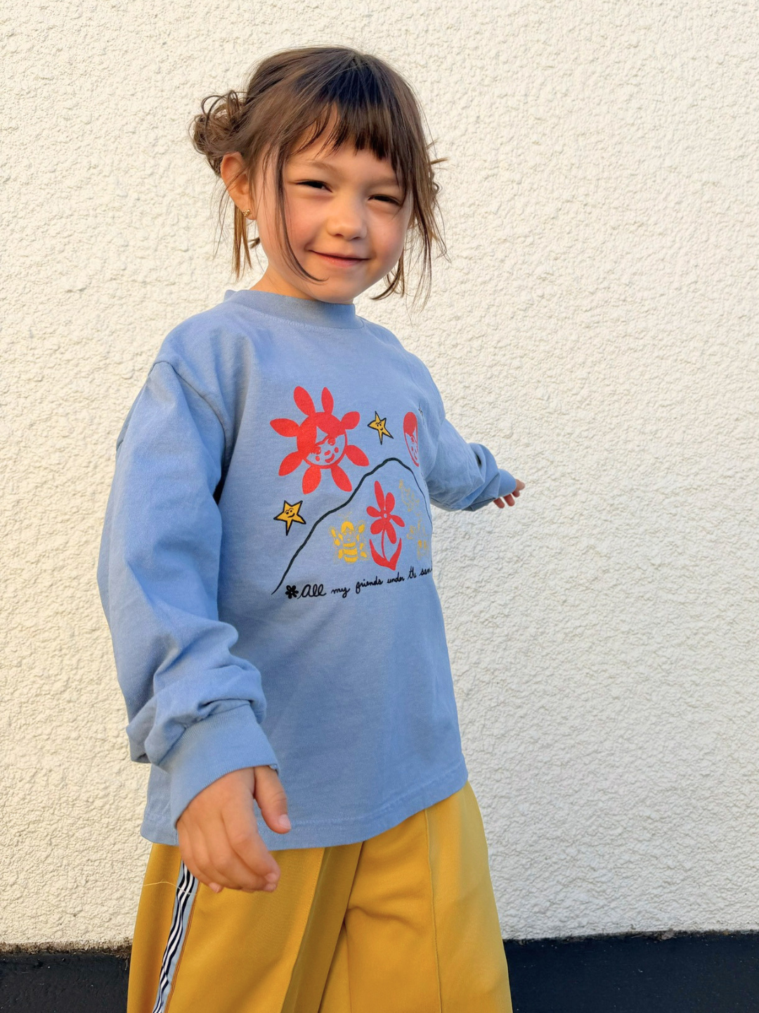 Child wearing a blue sweater with colorful designs against a white wall