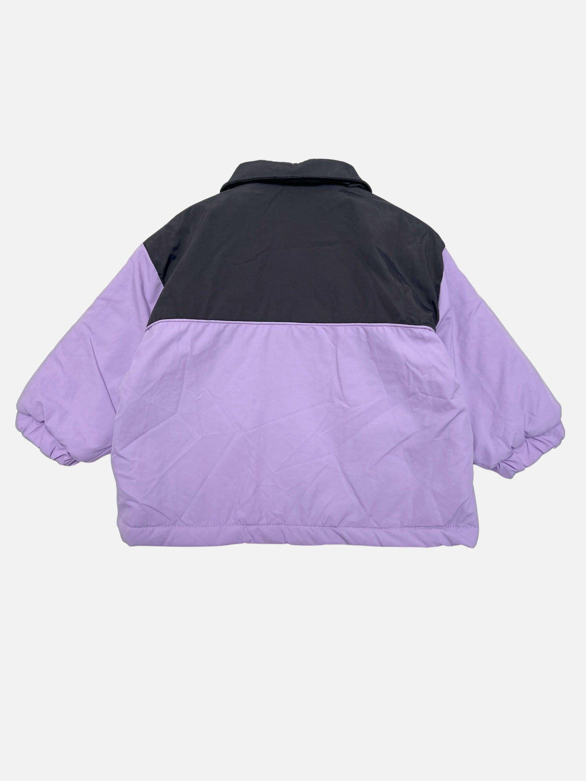A colorblock kids puffer jacket shown from the back, featuring a black upper back and shoulders with lavender purple sleeves and a lavender purple quilted body, set against a light gray background.