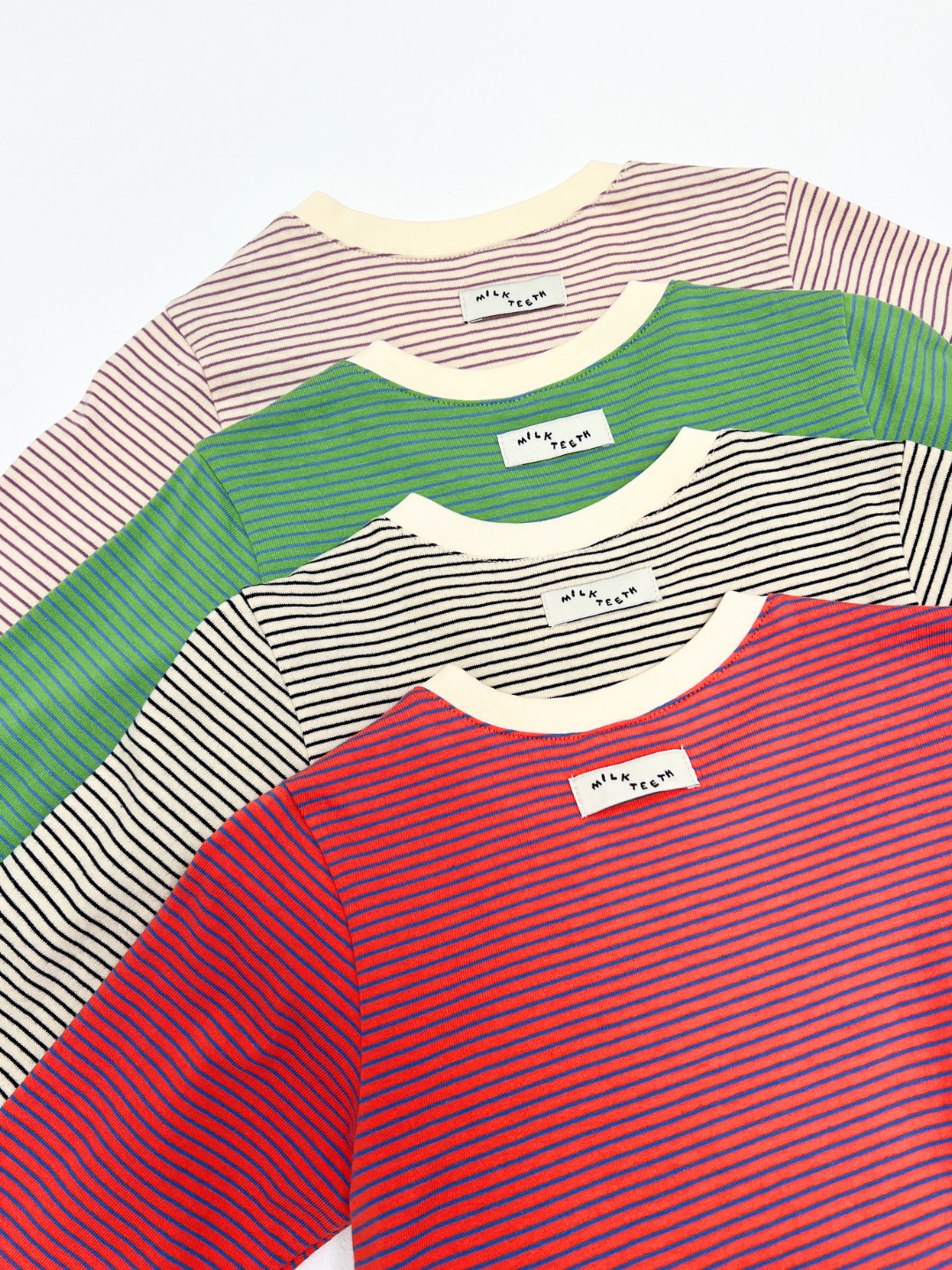 Four BABY STRIPE LONGSLEEVE shirts—crafted from soft cotton jersey in cream, green, beige, and red—are neatly fanned out in a stack, with each featuring a visible white neck tag for easy dressing. Perfect as a baby and toddler wardrobe basic.