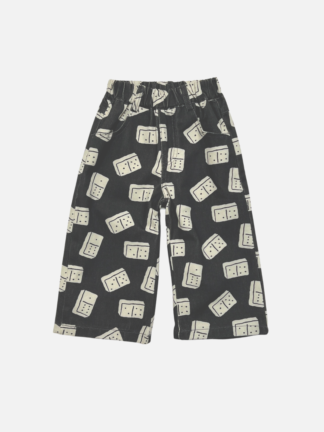 Black baggy kids printed jeans with an all-over cream domino pattern, featuring an elastic waistband, shown flat on a light gray background.