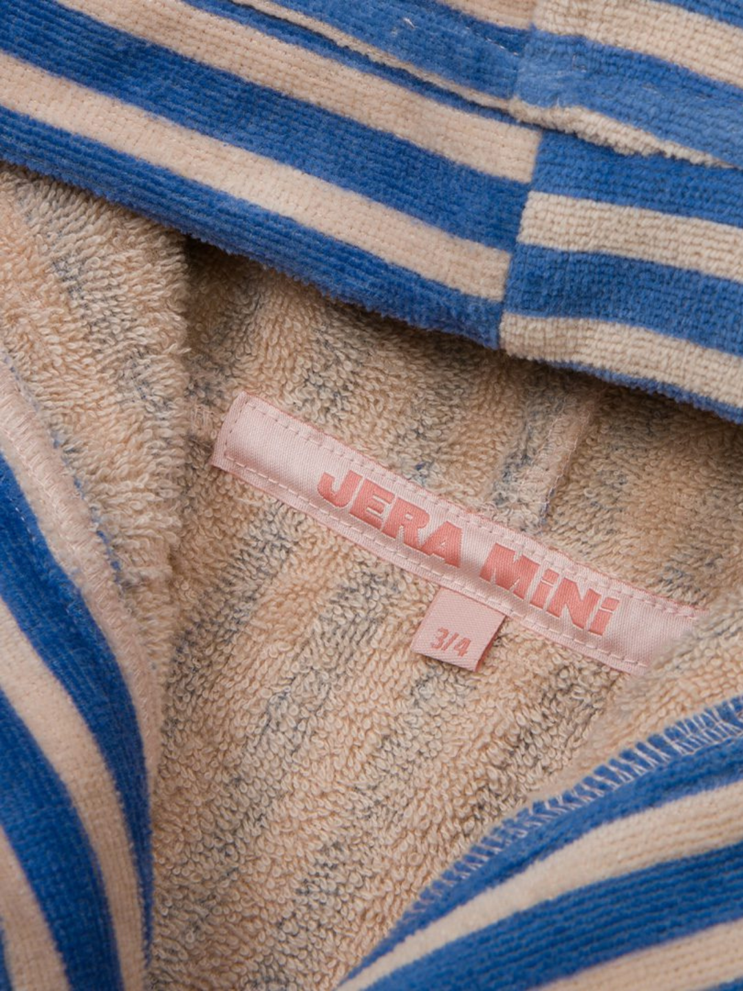 Pink | Close-up of the STRIPED ROBE in soft blue and beige cotton towelling with a pink "JERA MINI" label and size "3/4" tag. OEKO-TEX certified for comfort and safety.