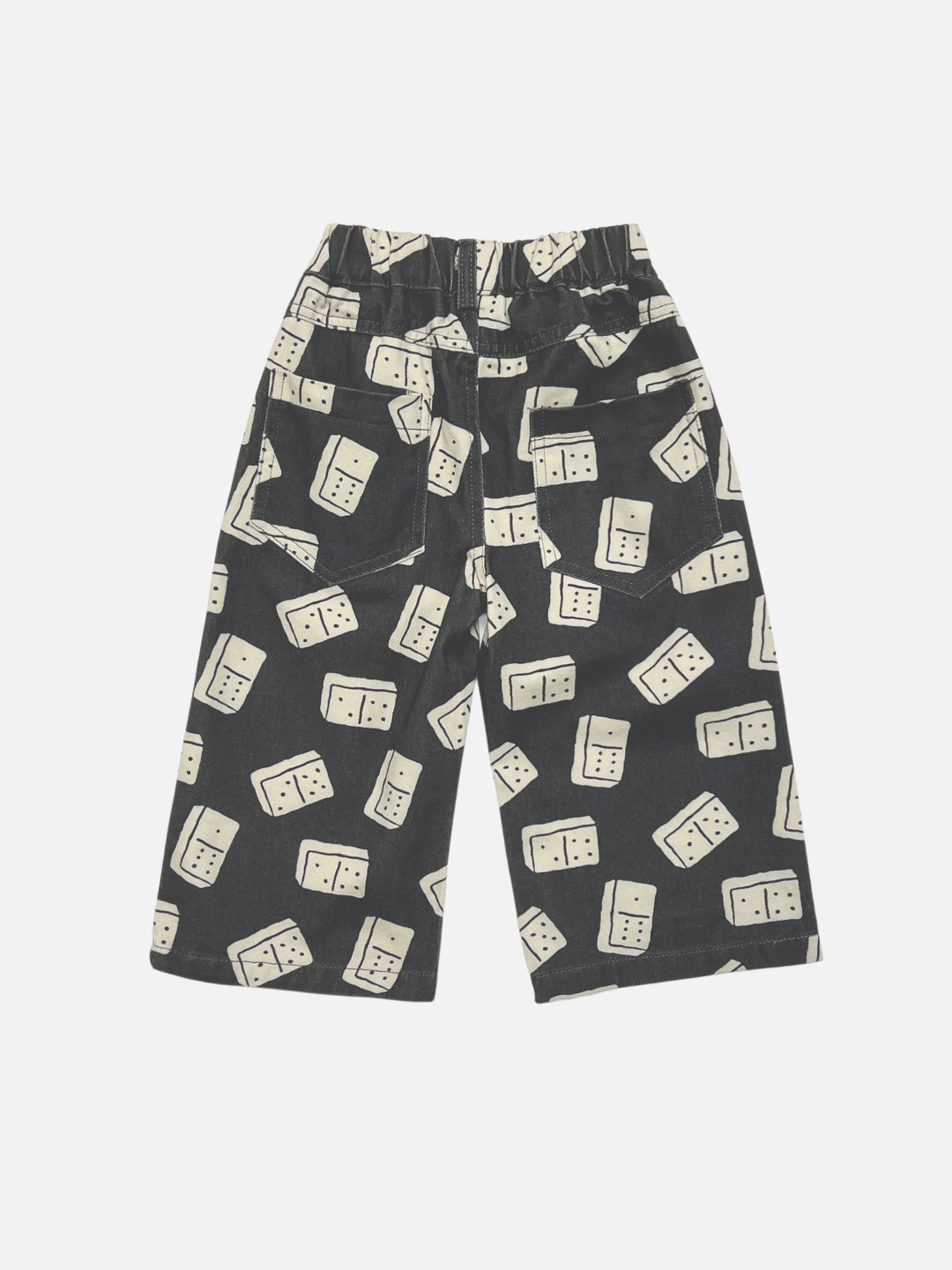 Back view of black baggy kids printed jeans with an all-over cream domino pattern, featuring an elastic waistband, shown flat on a light gray background. 