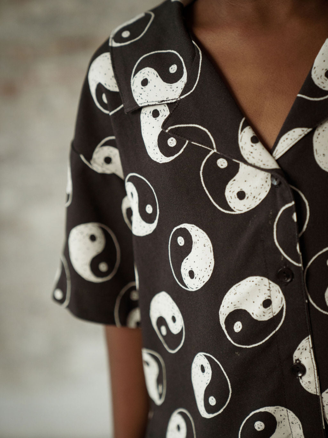 A zoomed in front view of the black button up shirt with a yin and yang pattern all over on a child.
