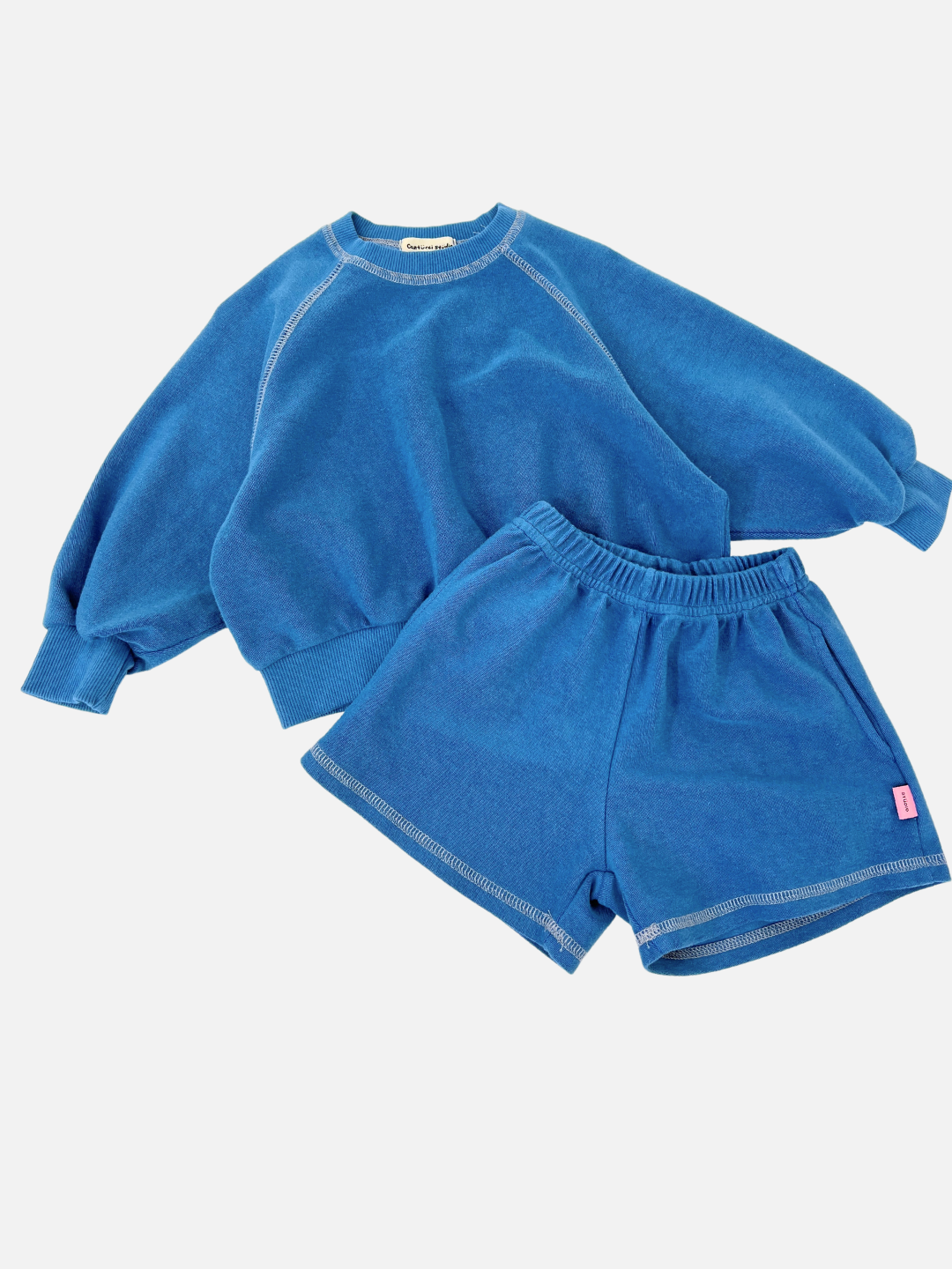 Blue | The blue sweatshirt and matching VARSITY SWEAT SHORTS set, featuring a vintage-inspired fit from a renowned Korean kids brand, is showcased laid flat. The brushed cotton shorts bring comfort and style to the ensemble.