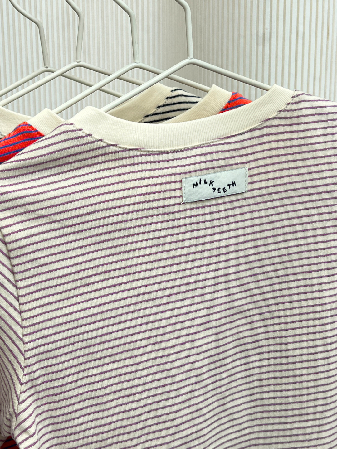 White/Purple | The BABY STRIPE LONGSLEEVE hangs on a rack with other shirts. Made from soft cotton jersey, this baby and toddler essential features thin purple stripes and a white collar for easy dressing.