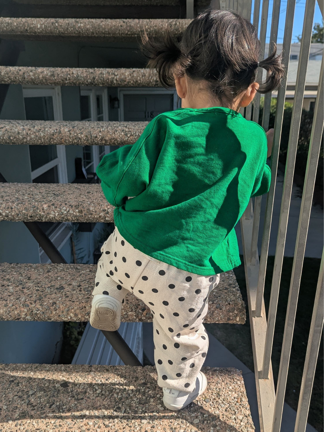 Child in a green shirt and polka dot pants standing on a staircase.