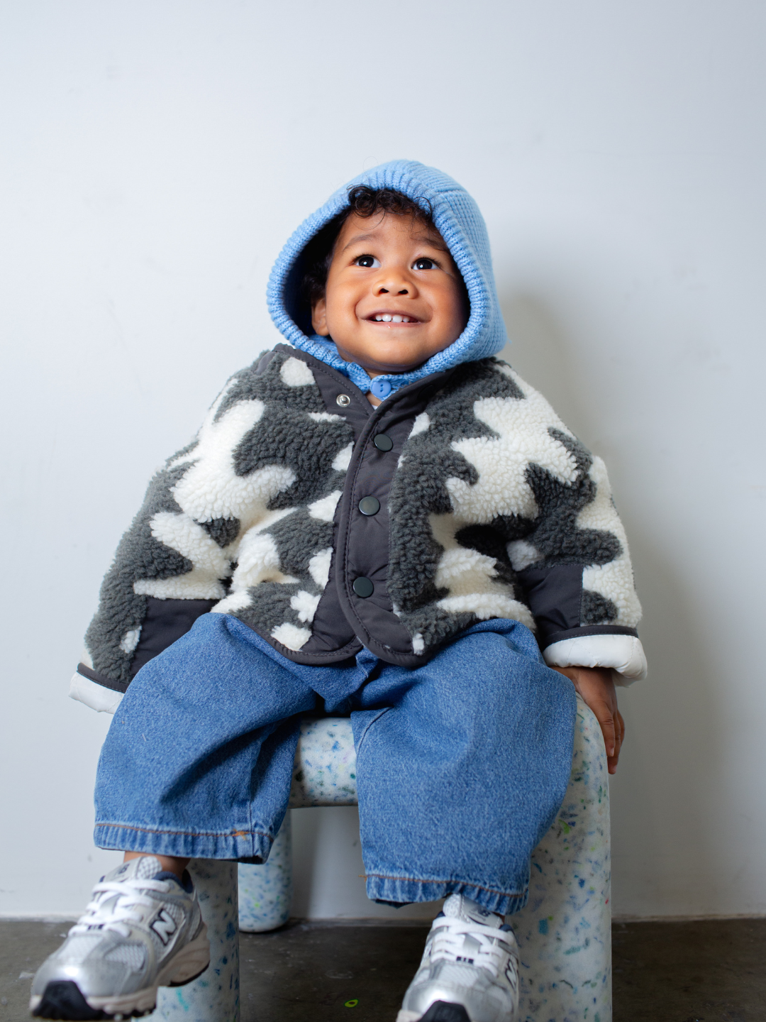 Dark Wash | Child wearing a patterned jacket and blue jeans sitting on a chair against a white wall.