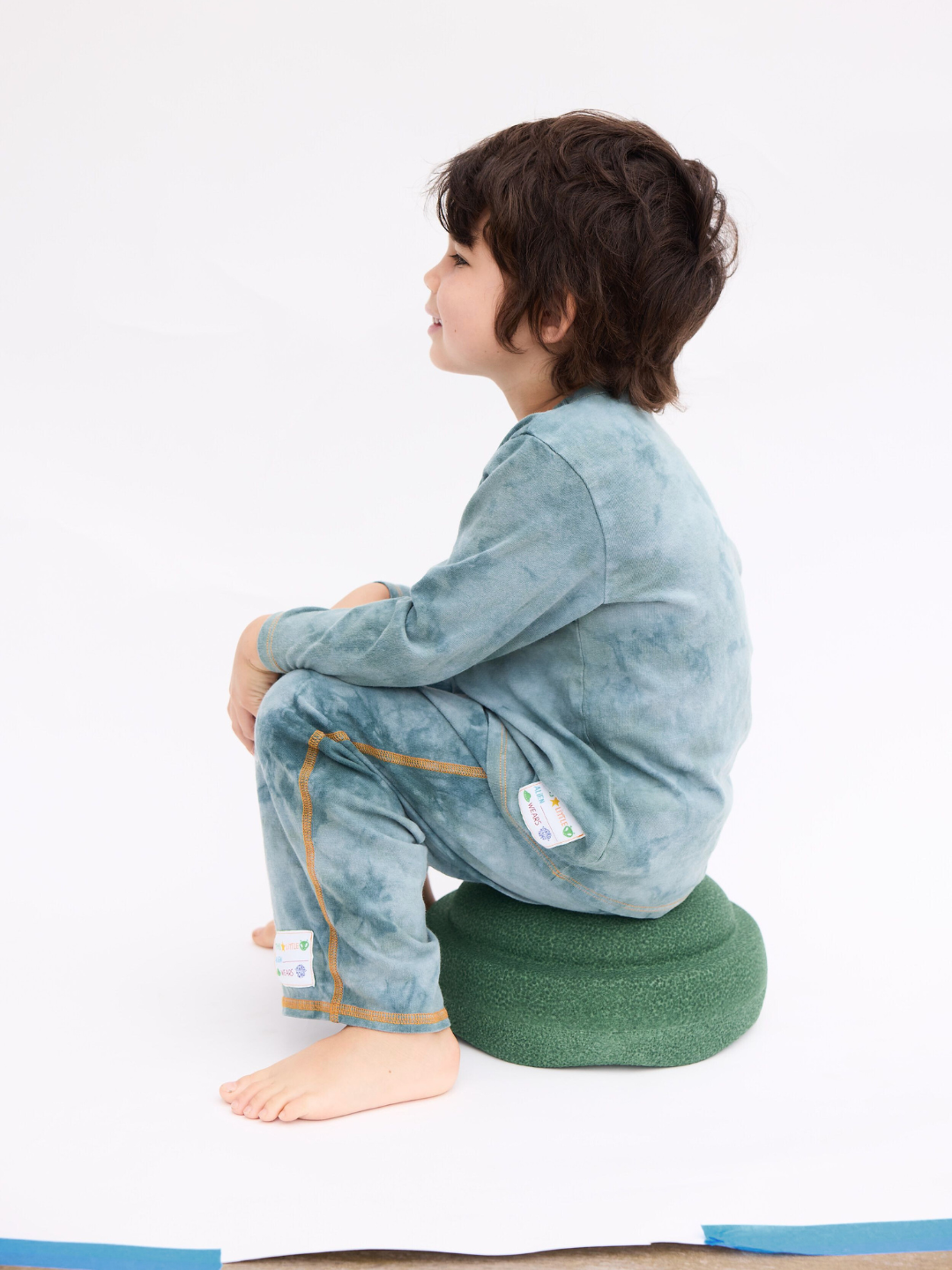 Sage | The COSMO TIE DYE PANT in sage, worn by a child with the matching long sleeve tee, sitting on a green stool on a white backdrop.