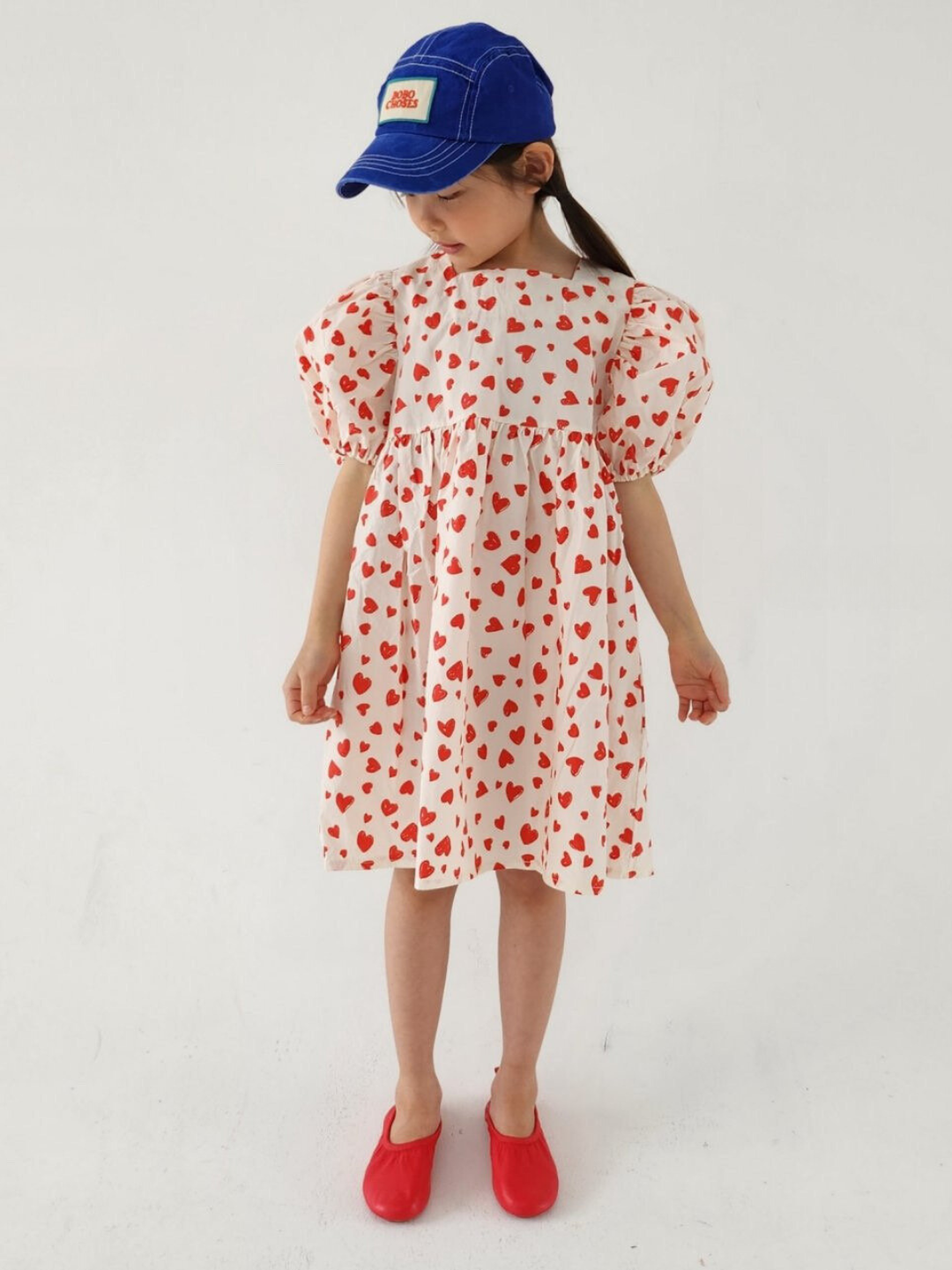 A child wearing a kids' puff-sleeved dress with red hearts on a white background