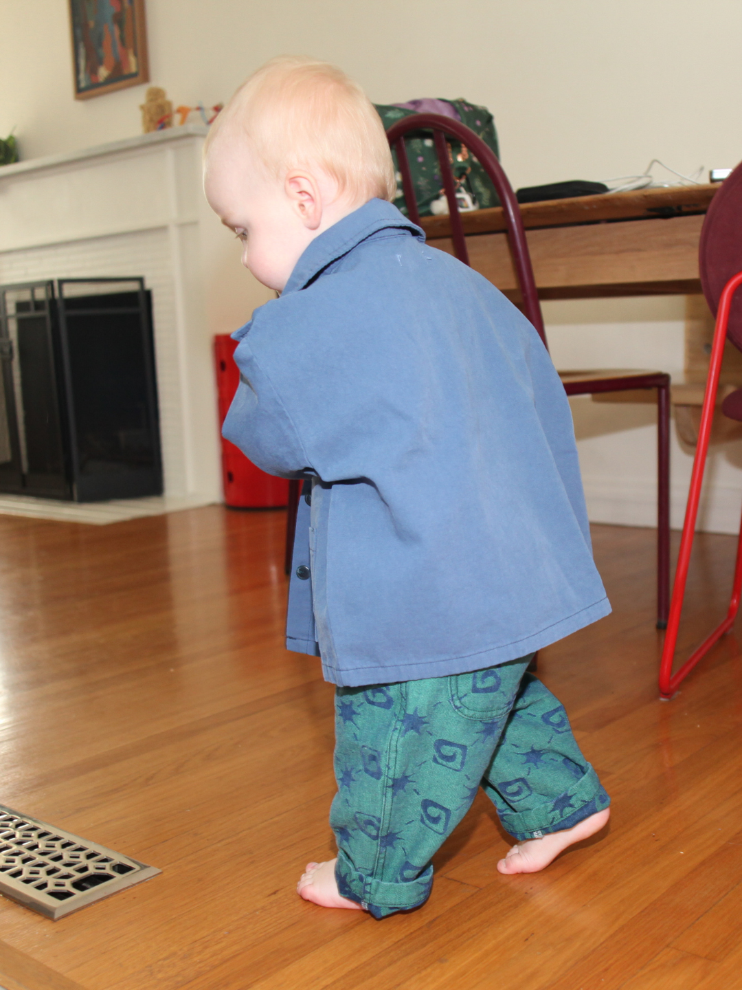 Blue | Child wearing a blue coat and green pants with blue patterns on a wooden floor.