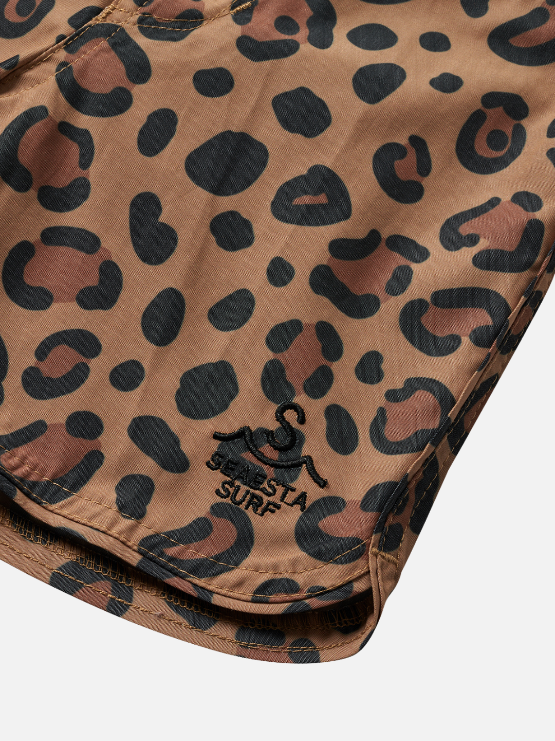 Close-up of brown leopard print fabric showcases a logo with an octopus and "SIESTA SURF" on the edge, echoing the retro feel of CALICO CRAB BOARDSHORTS.