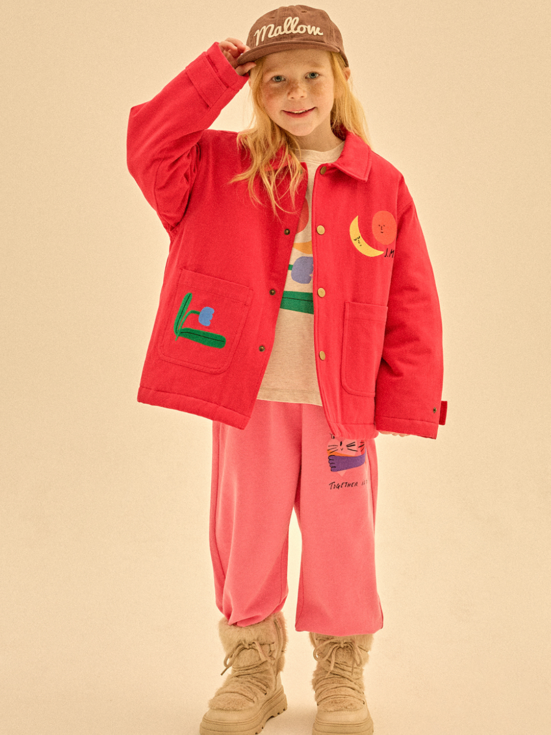 A child beams in the COLORED NATURE JACKET, pink pants, tan boots, and a brown cap—ready for fun 