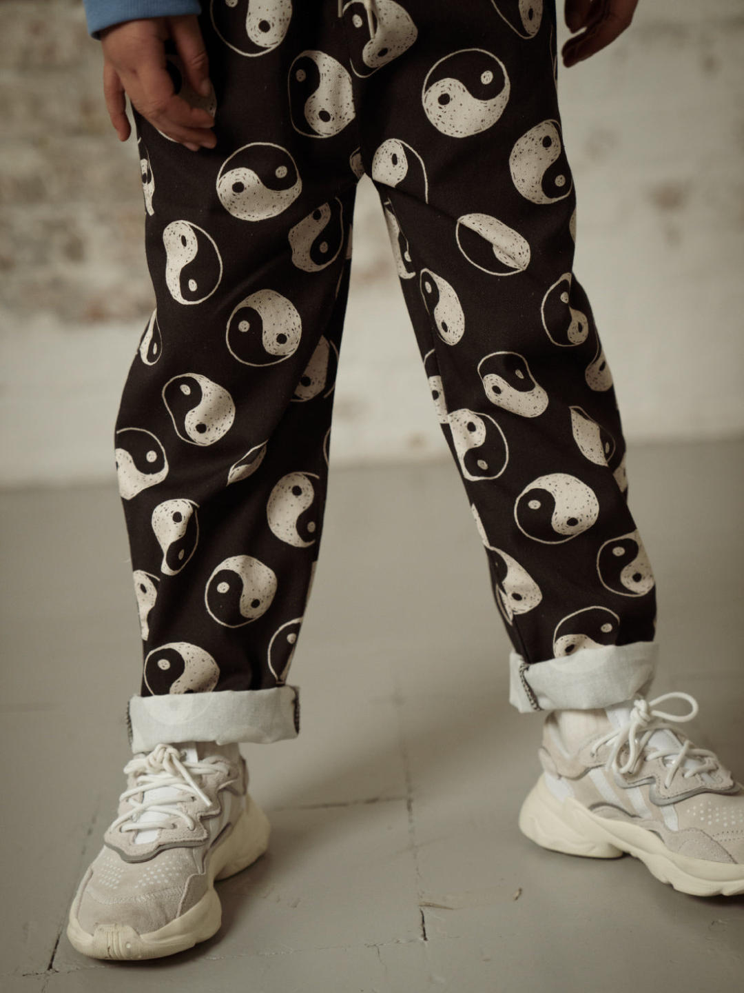 A zoomed in front view of the drawstring black pants with a yin and yang pattern all over on a child with the ankles cuffed.