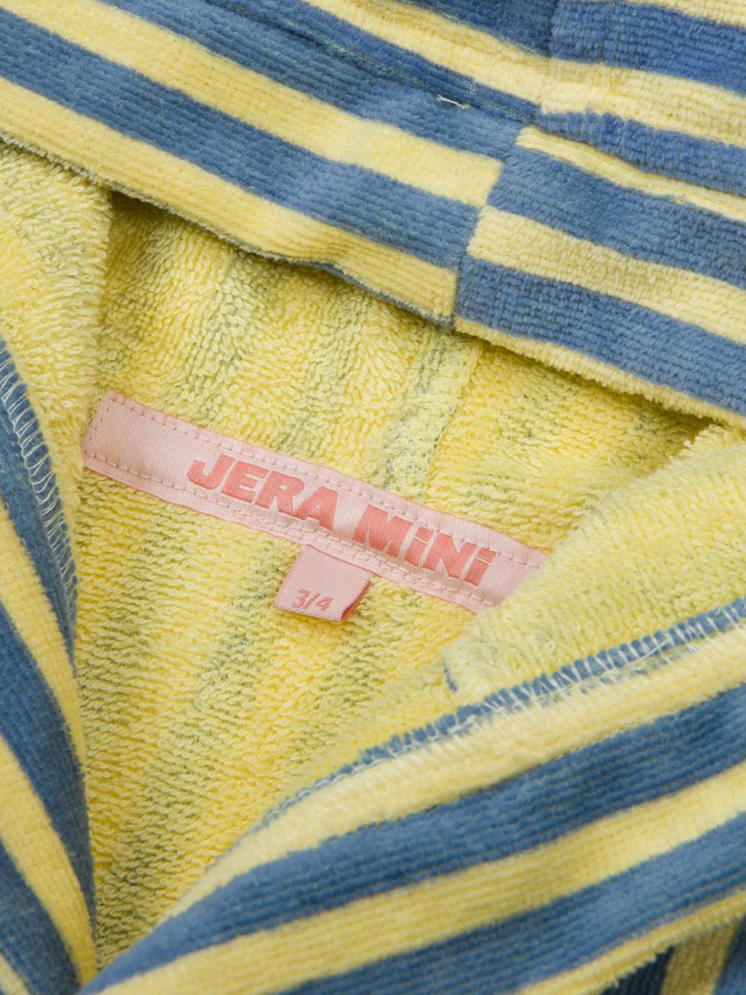 Close-up of the STRIPED ROBE in yellow and blue towelling cotton, featuring a pink "JERA MINI" label and a size tag marked "3/4".