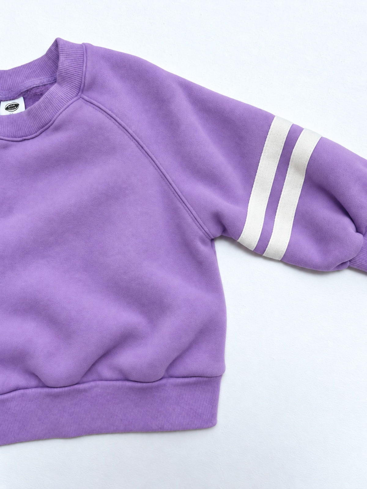Purple | Detail view of kids crewneck sweatshirt in violet purple with two white stripes on each sleeve