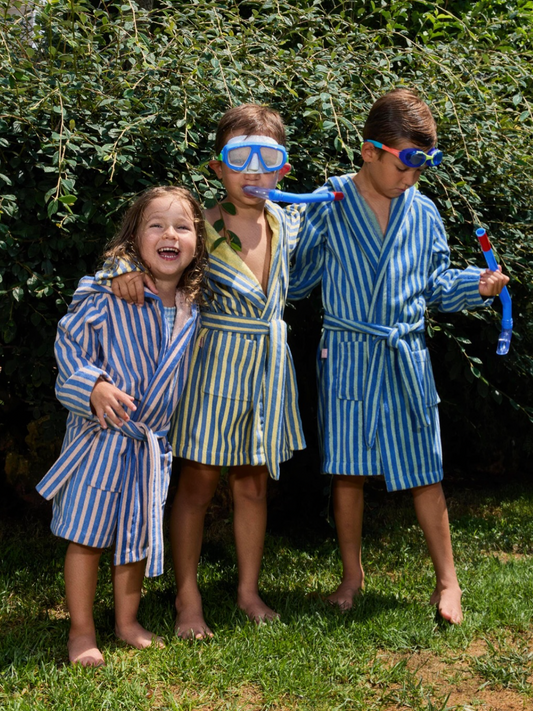 Second image of Pink | The STRIPED ROBE is a children’s towelling bathrobe with blue and beige vertical stripes, made from velvety-soft cotton. It features front pockets, a matching tie belt, and is OEKO-TEX certified—shown on a white background.