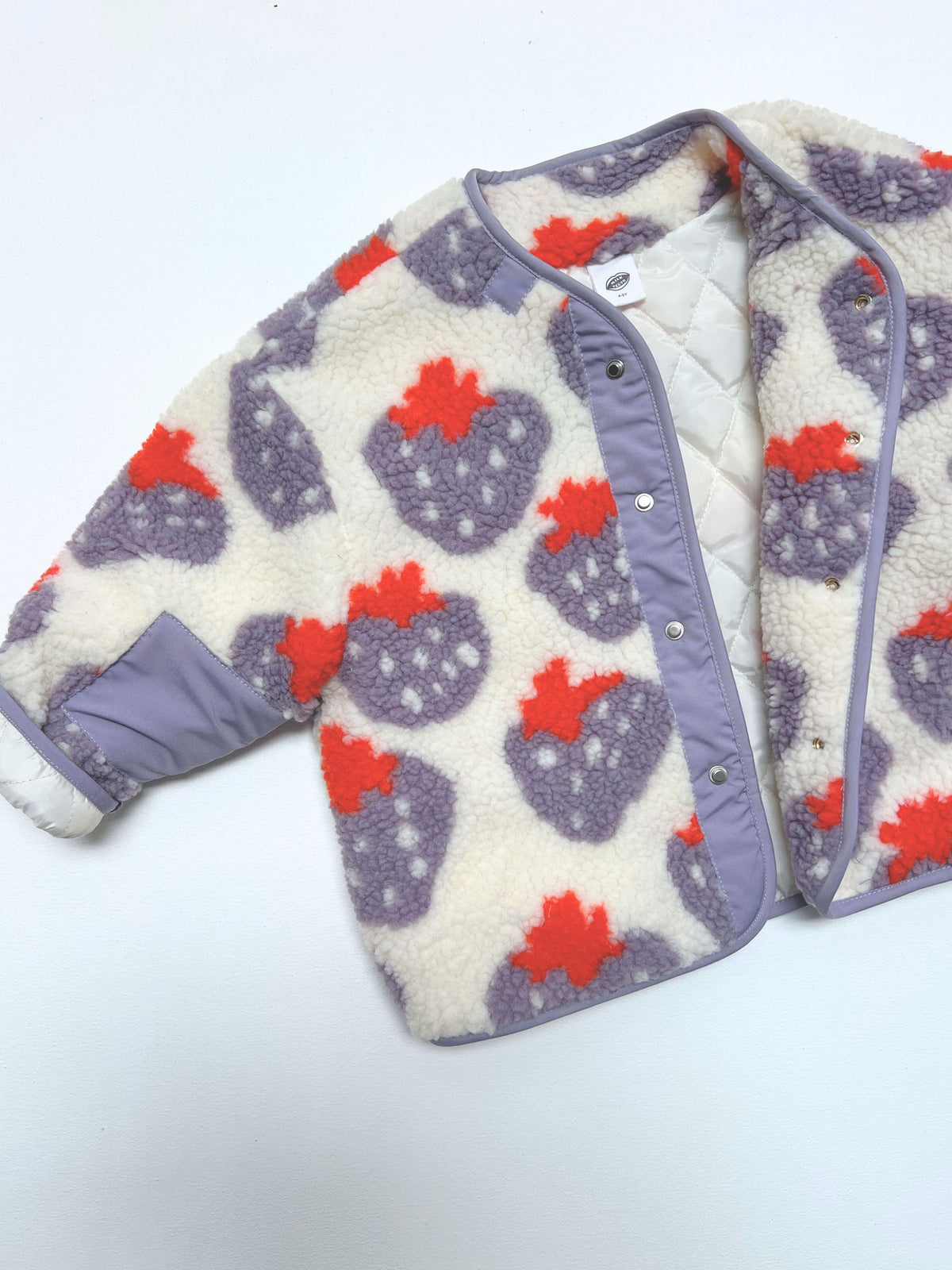 Front view of kids collarless sherpa jacket in cream fleece patterned all over in a purple and red strawberry print, with front snap closure open to show white quilted lining.