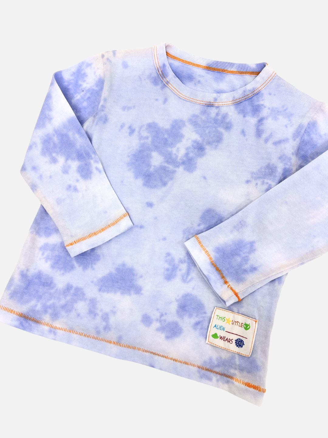 Discover the KOKO MOMO LONGSLEEVE, a blue tie-dye long-sleeve shirt with orange stitching, adorned with a small patch that reads "This little alien wears." Check out our product-specific size chart to find your perfect fit.