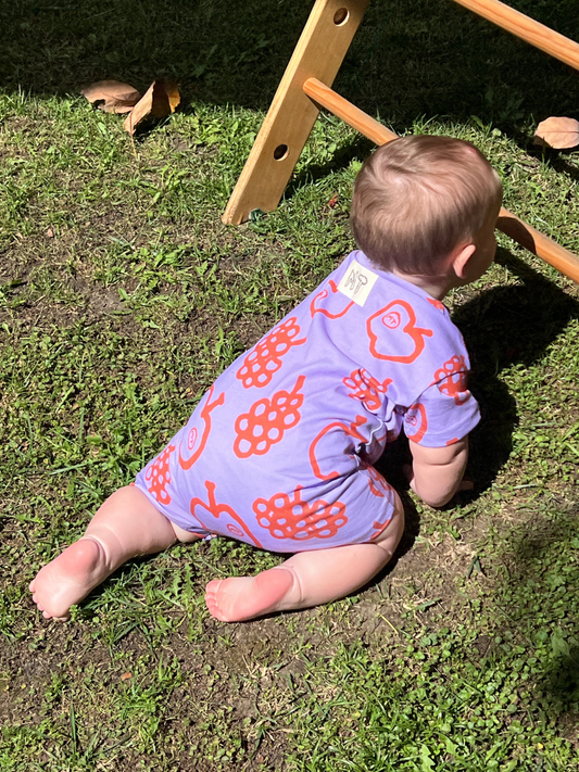 Second image of The FRUIT STAND ROMPER is a lavender short-sleeve organic cotton baby outfit with orange apple and grape fruit prints, perfect for summer, shown on a white background.