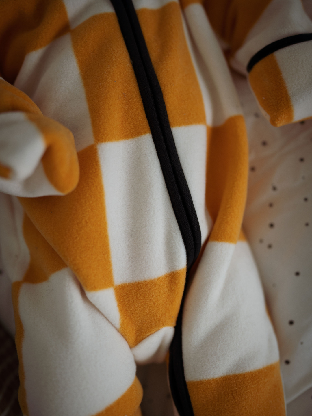 Detail of the zipper on a one piece stroller suit with a bold apricot and white checkerboard 