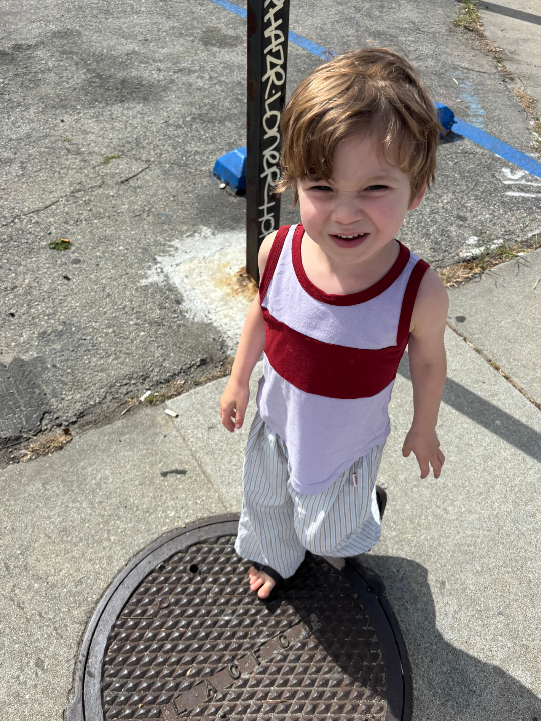 Blue | Child in the poplin stripe pants in light blue, and a lavender and red tank top, standing on a sidewalk