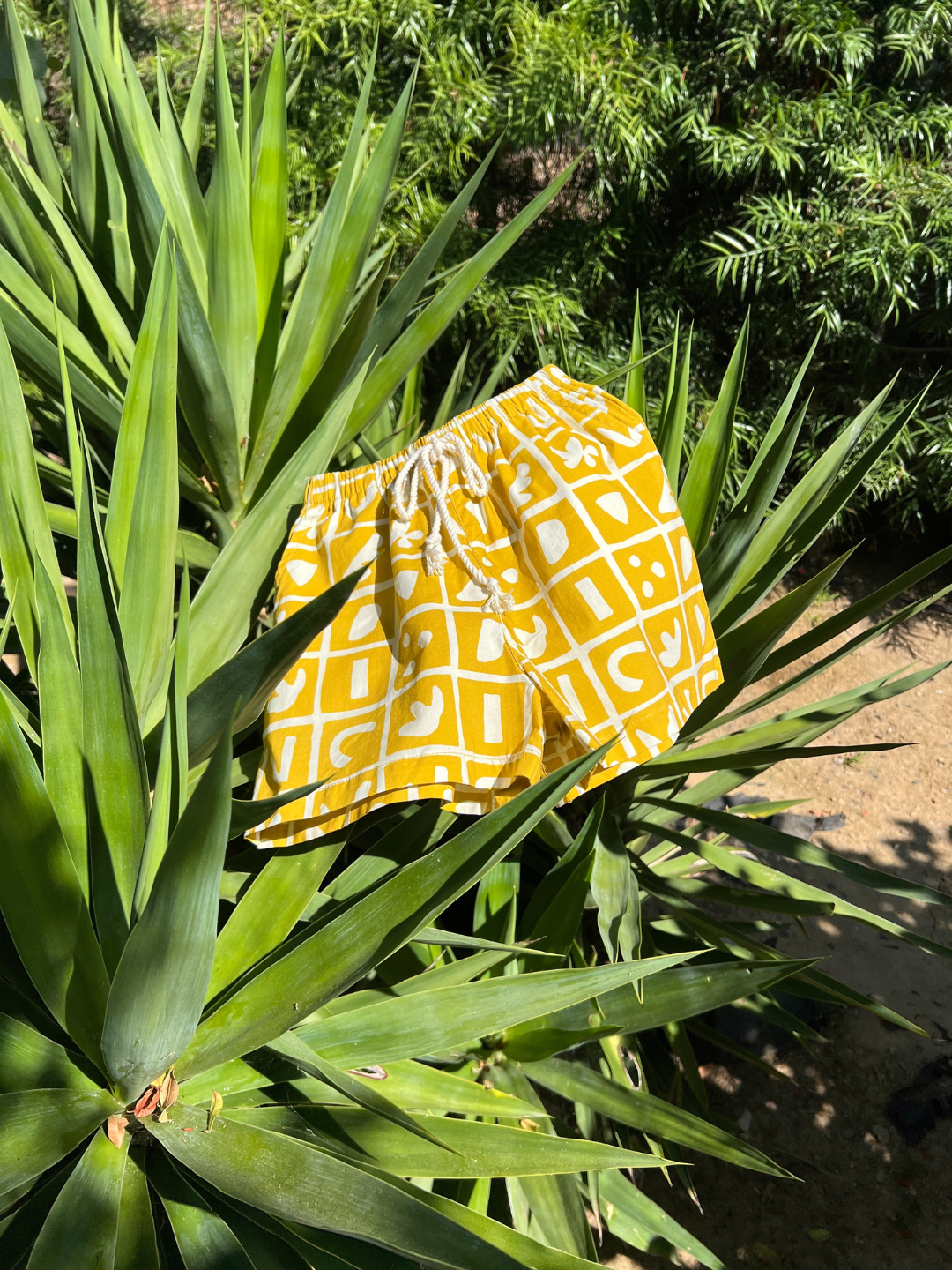 Mustard | A pair of kids' shorts drying on a plant. Mustard yellow overlaid with a grid of different shapes in white