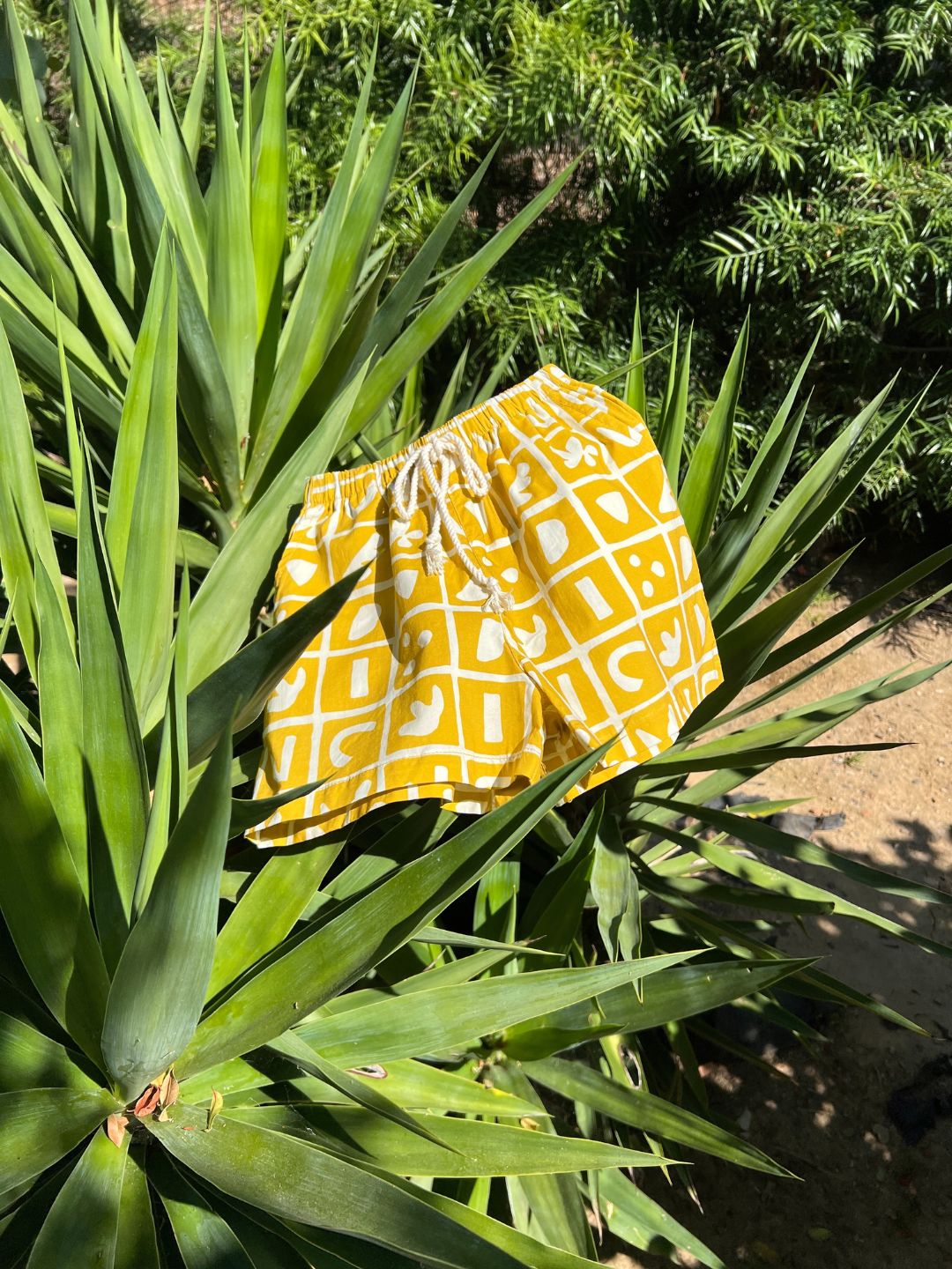 A pair of kids' shorts drying on a plant. Mustard yellow overlaid with a grid of different shapes in white