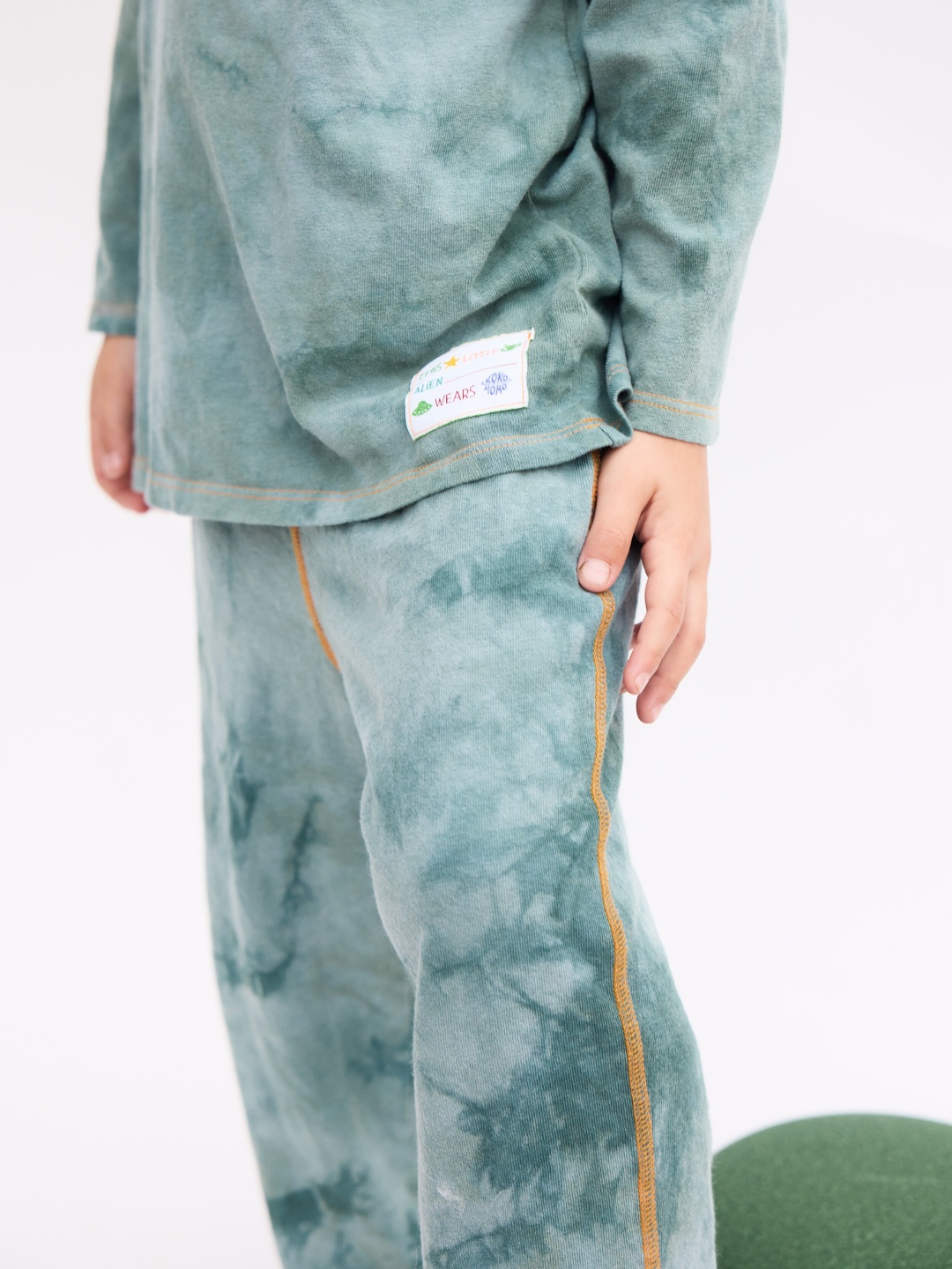 The COSMO TIE DYE LONG SLEEVE in sage, a crewneck tee worn by a child with the matching pants, standing on a white backdrop.