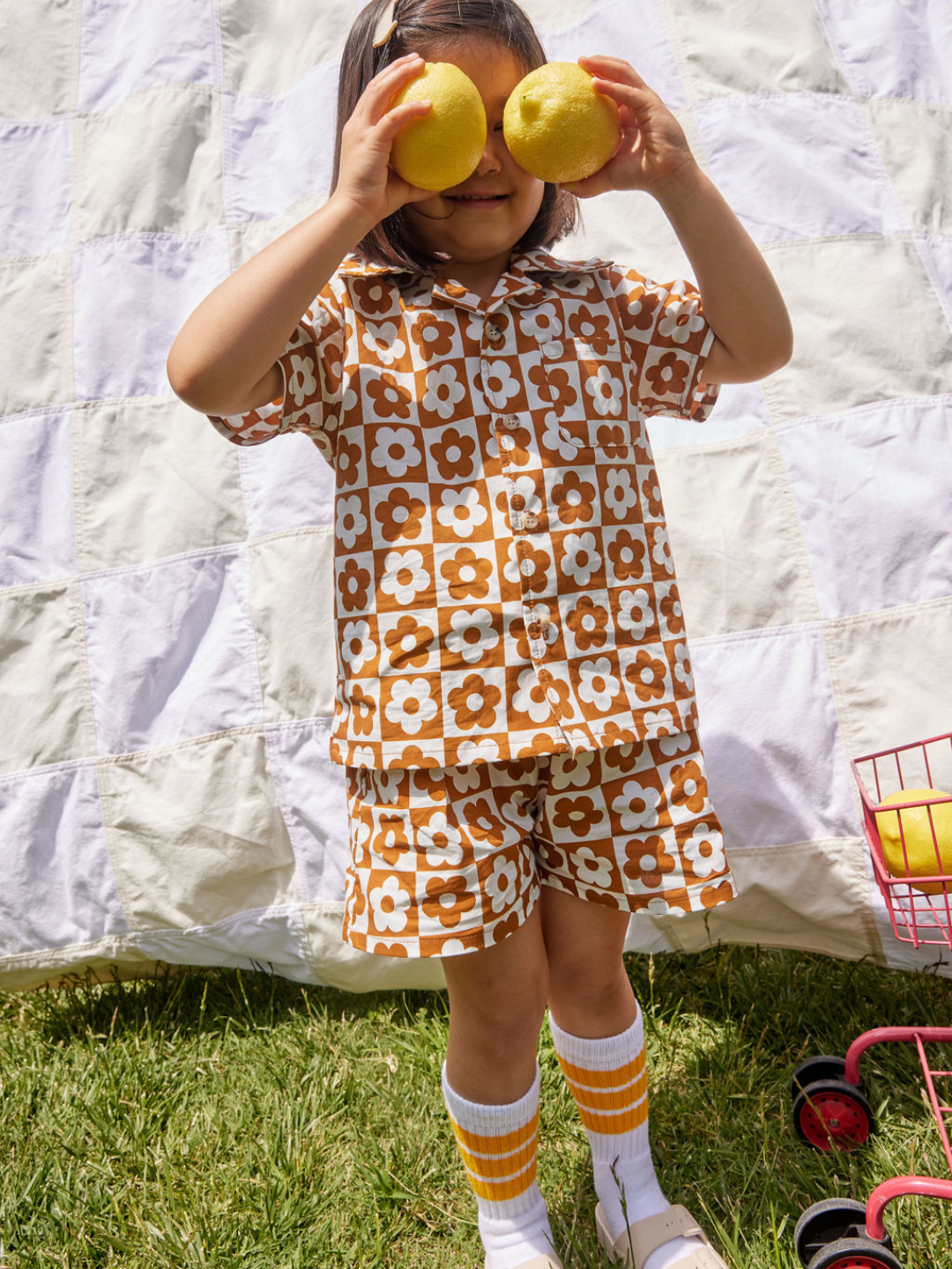 Child posing with lemons wearing a kids' short set in a checkerboard pattern of terracotta and white flowers