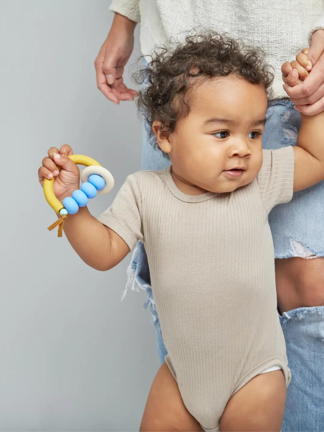 Pacific | Baby holding teether with white ring on yellow semicircle, sky blue beads strung along top